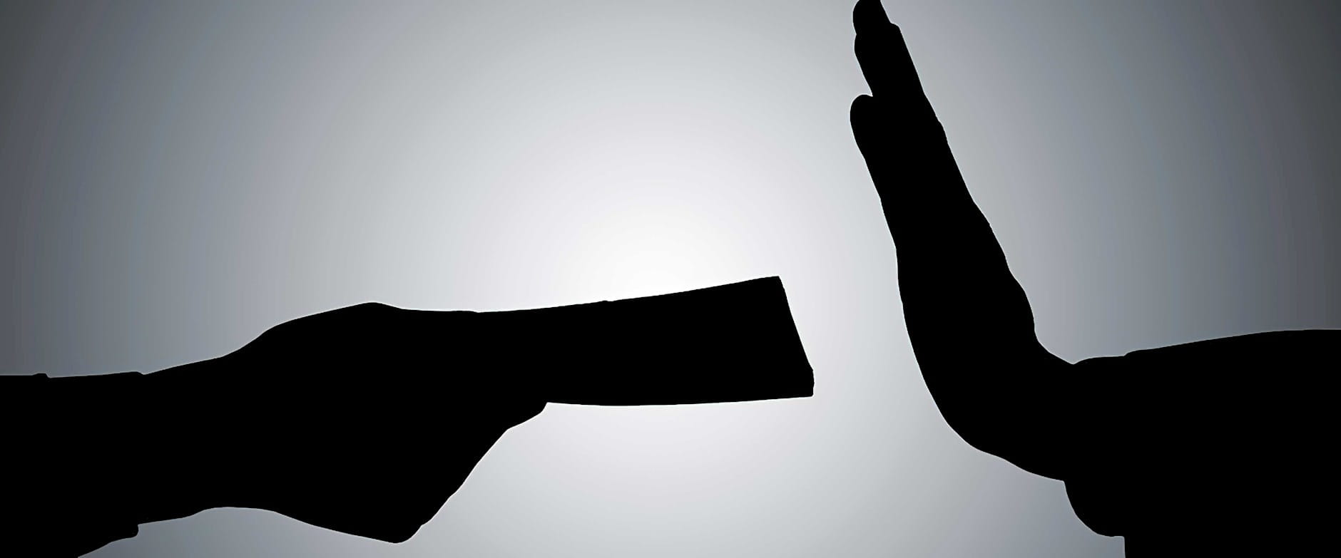 Silhouette of a person's hand giving money to another person with their hand in a stop gesture