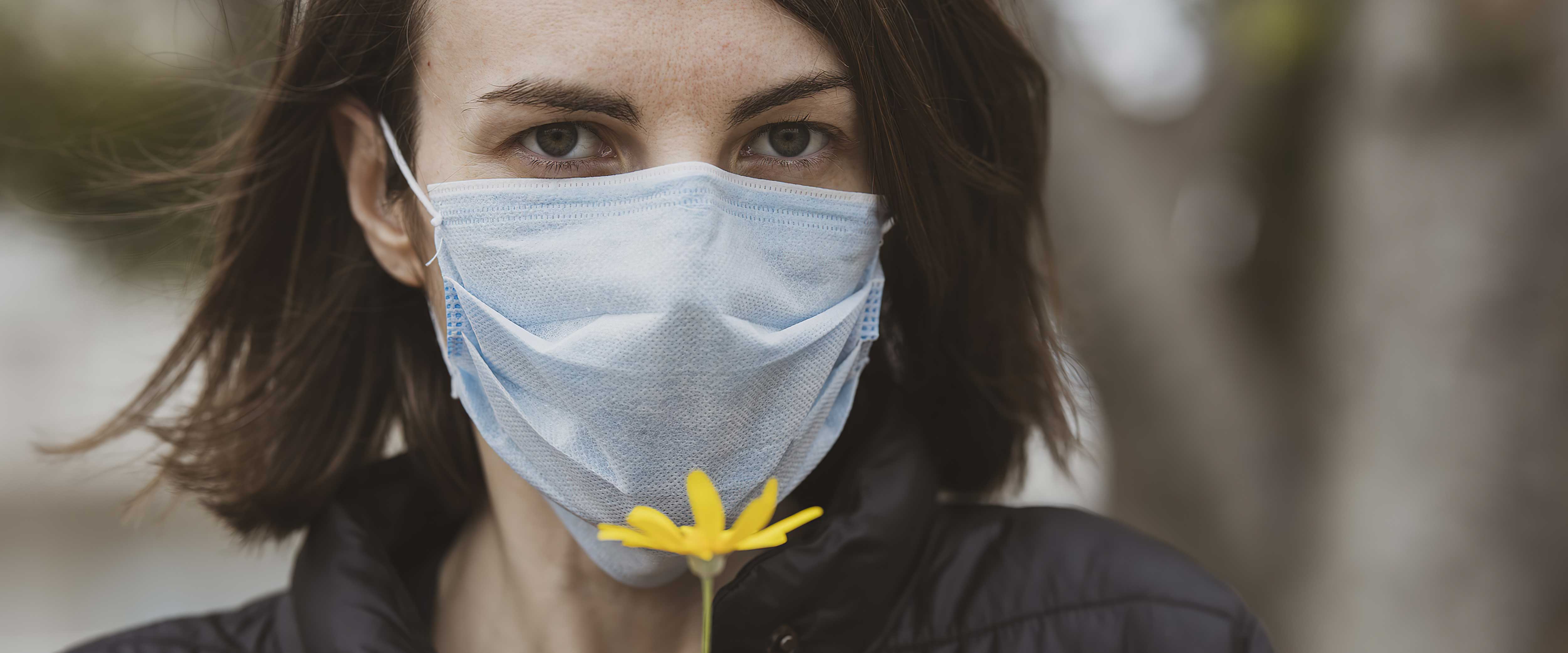 Woman in PPE mask holding up blooming flower