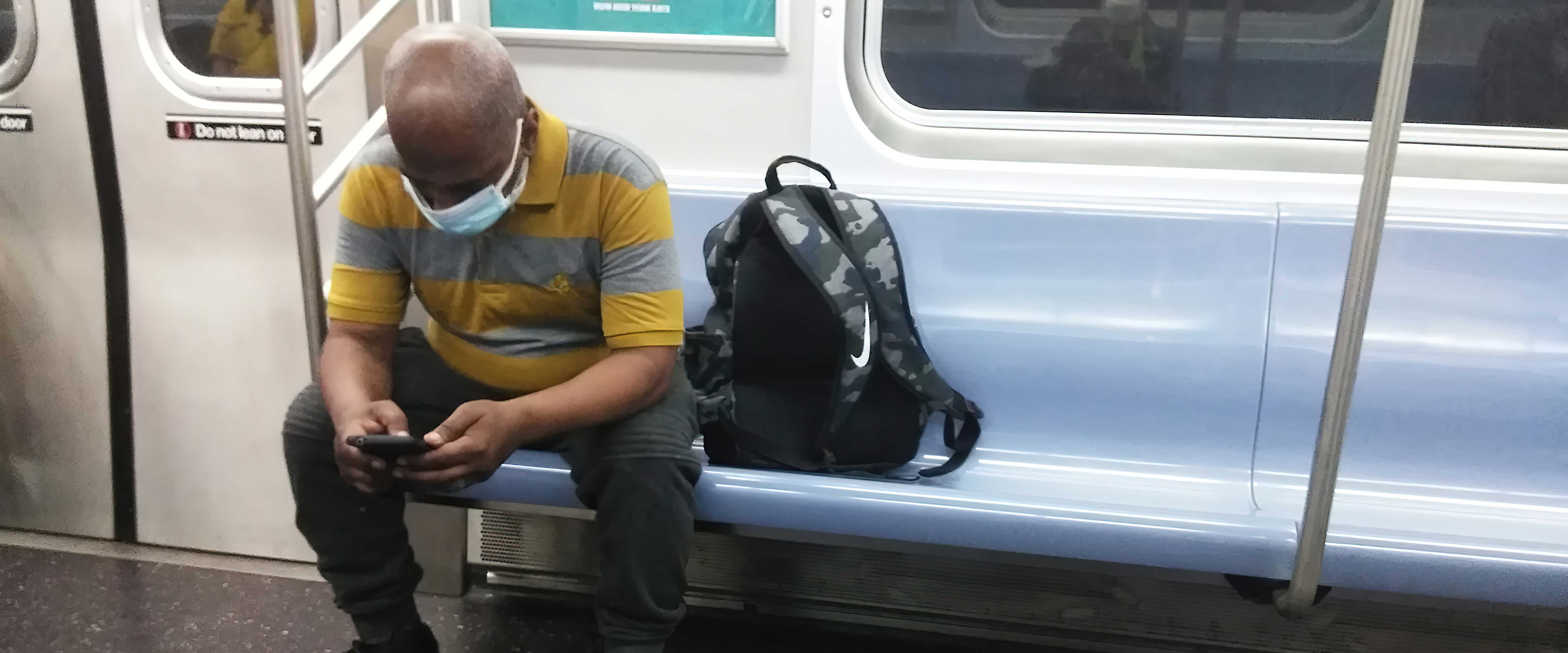 Man in mask riding MTA subway looking down at phone