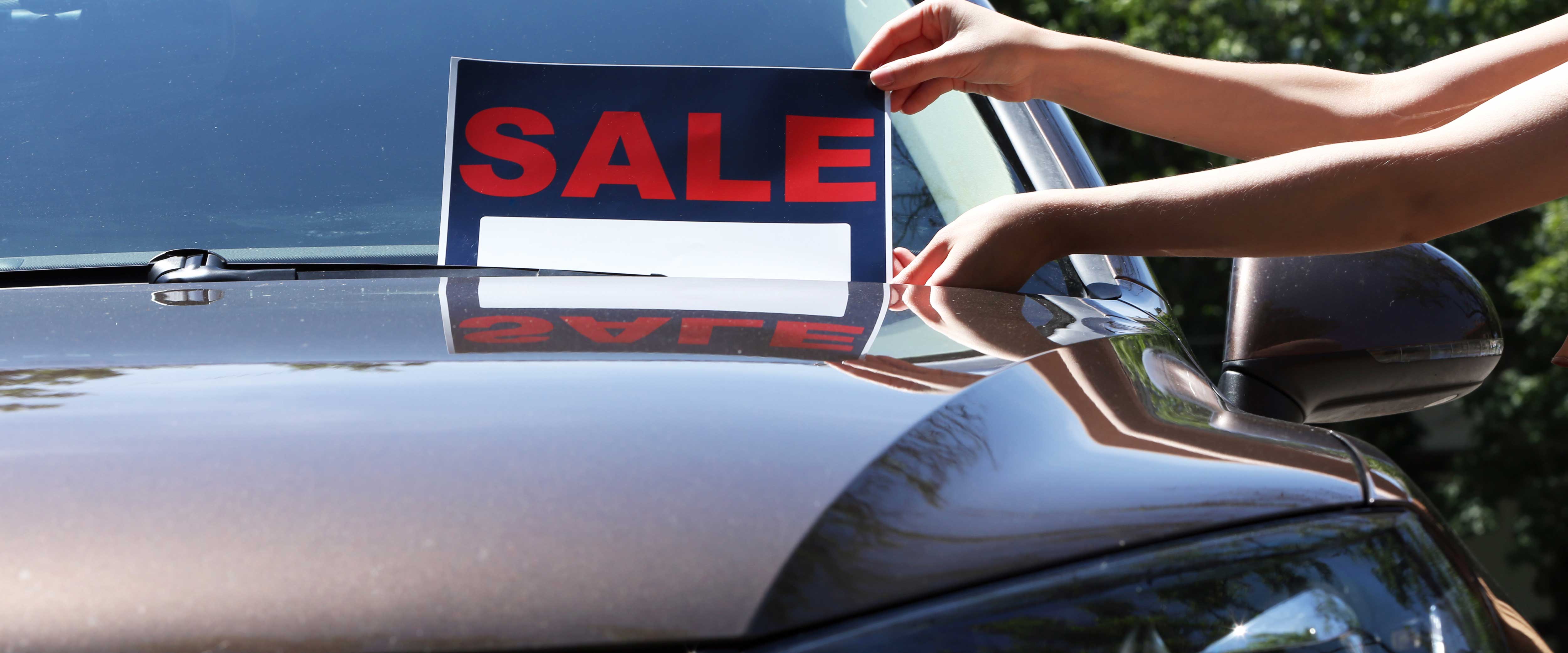 Hands placing a for-sale sign on the windshield of a car