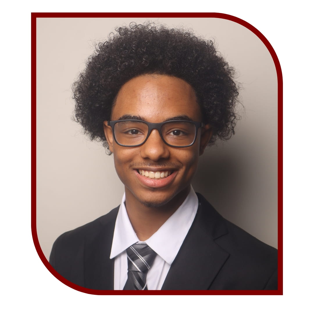 Picture of smiling curly-haired man wearing a suit and glasses. The picture is bordered by a maroon frame. 