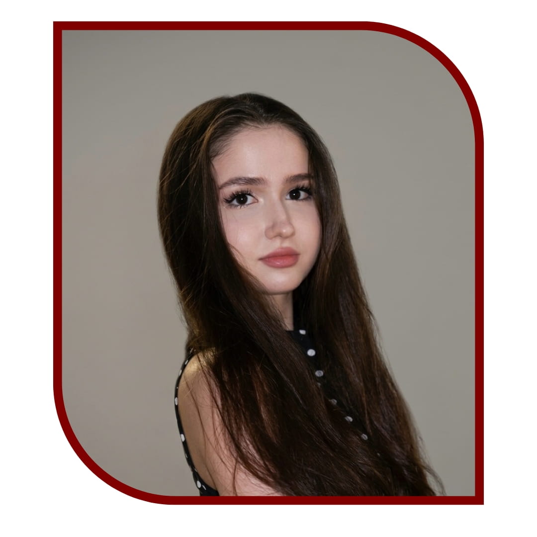 Picture of a dark-haired woman standing in front of a grey background. The picture is bordered by a maroon frame.