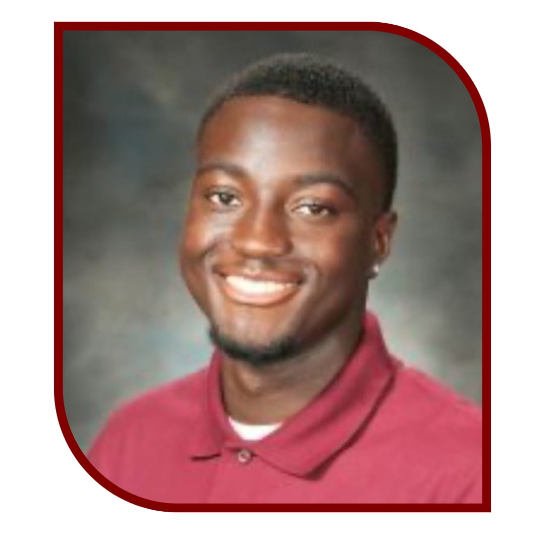 Picture of a smiling man wearing a red shirt and standing in front of a grey background. The picture is bordered by a maroon frame.