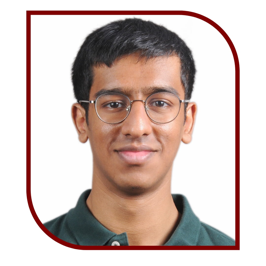 Picture of a dark-haired man wearing a green shirt and glasses and standing in front of a white background. The picture is bordered by a maroon frame.