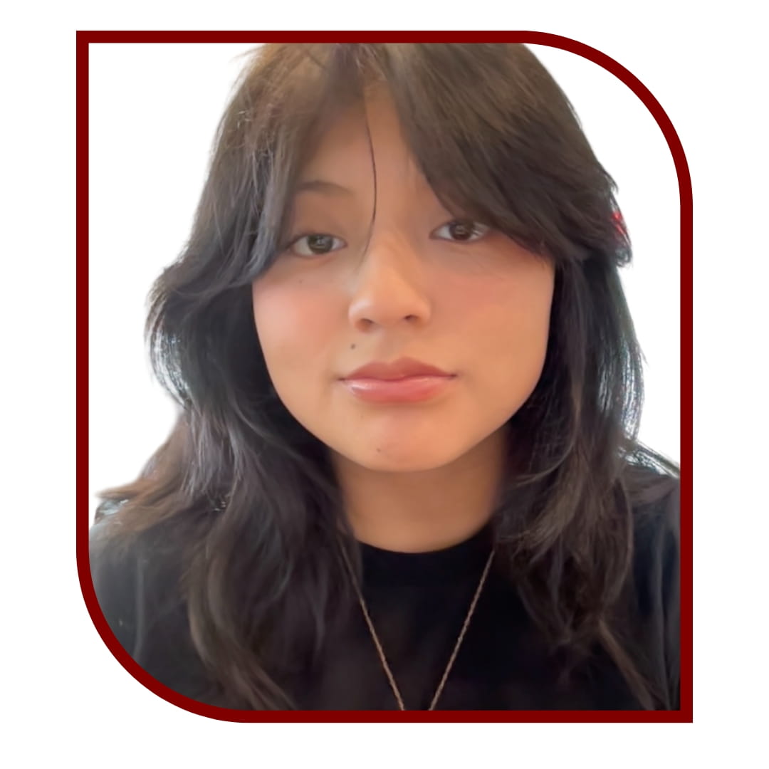 Picture of a smiling dark-haired woman wearing a black shirt and standing in front of a white background. The picture is bordered by a maroon frame.