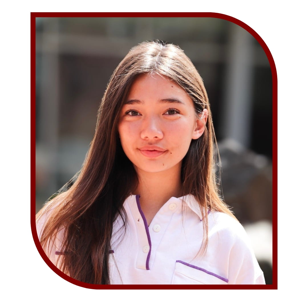 Picture of a smiling brown-haired woman wearing a white shirt and standing in front of a blurred background. The picture is bordered by a maroon frame.