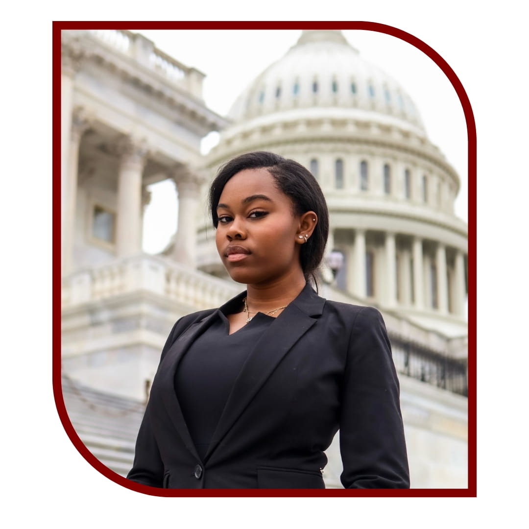 Picture of young dark-haired woman wearing a black business outfit standing in front of the capitol. 