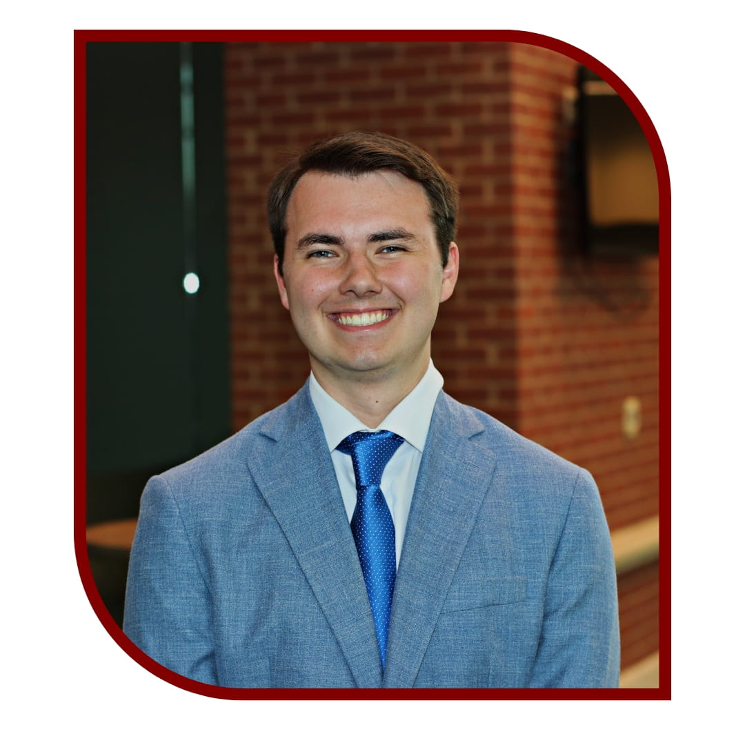 Picture of young smiling man wearing a blue tux. The photo is bordered by a maroon frame. 