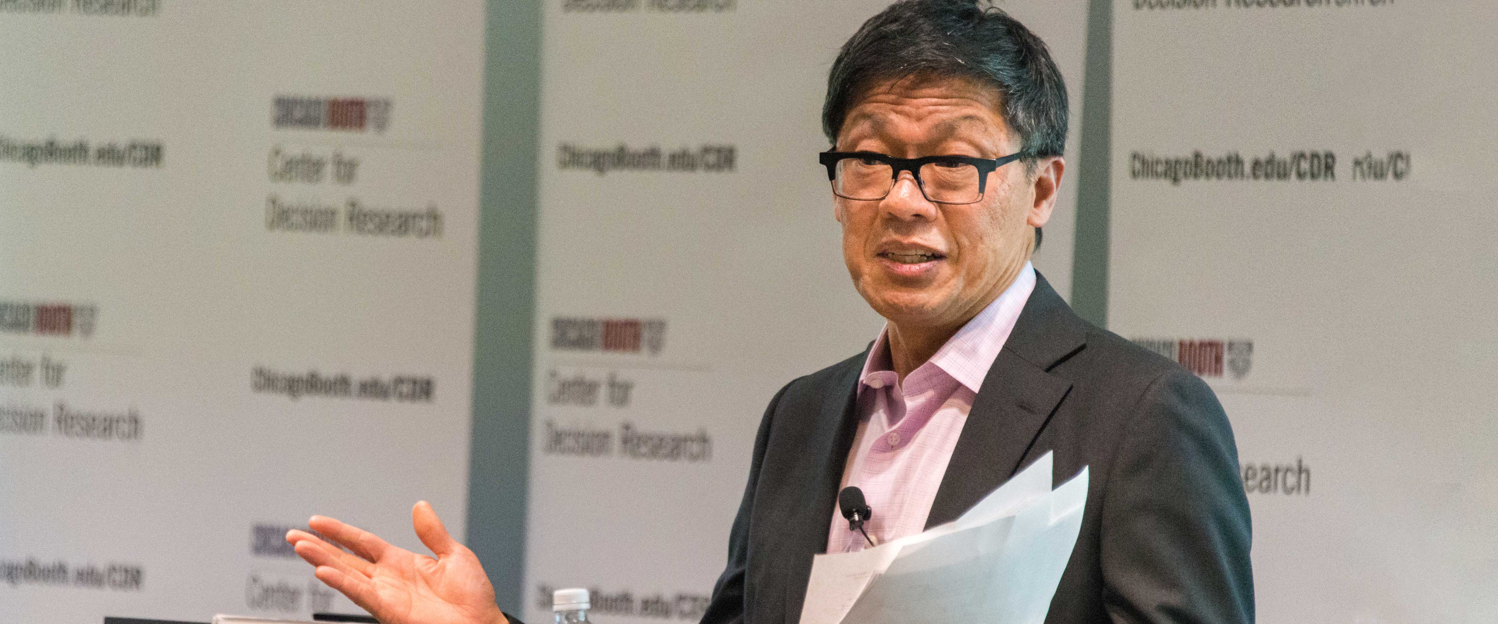 George Wu speaking in front of a CDR backdrop holding papers