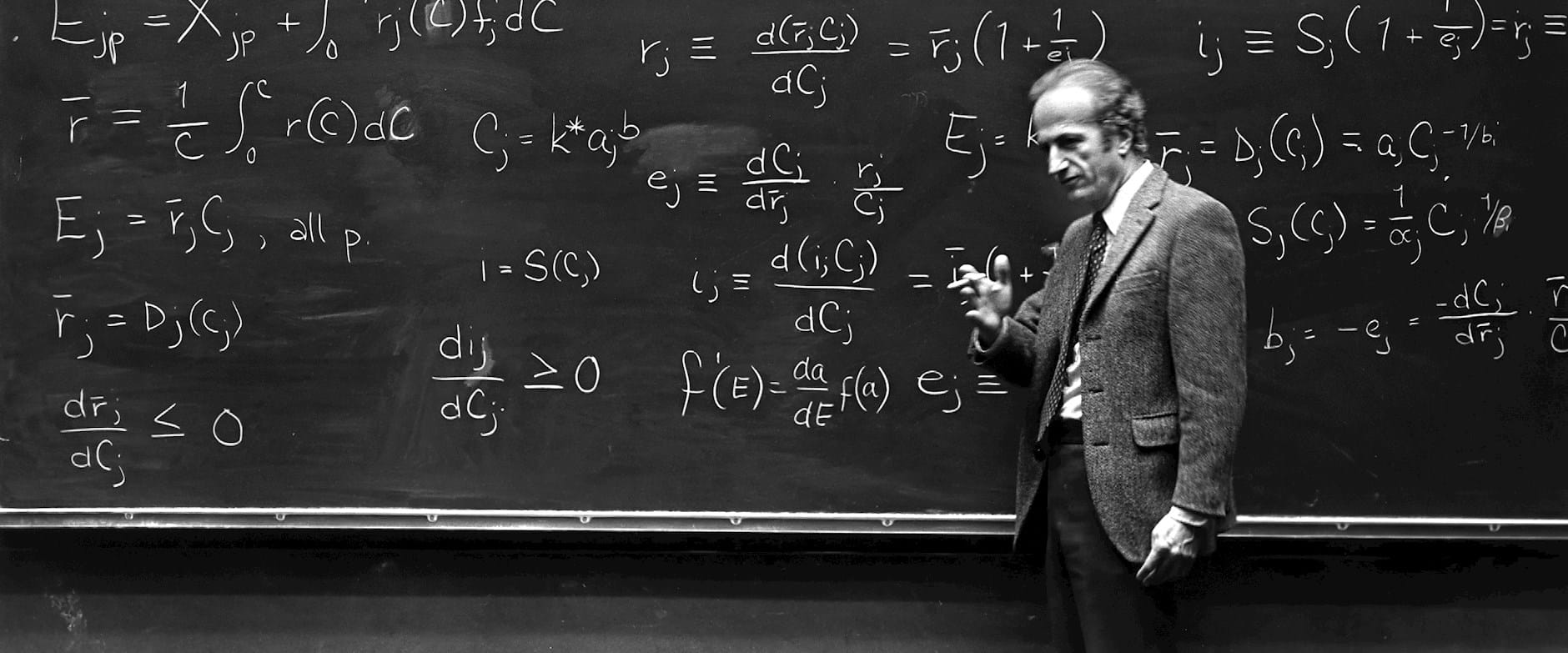Gary Becker teaching in front of a large chalkboard covered in equations