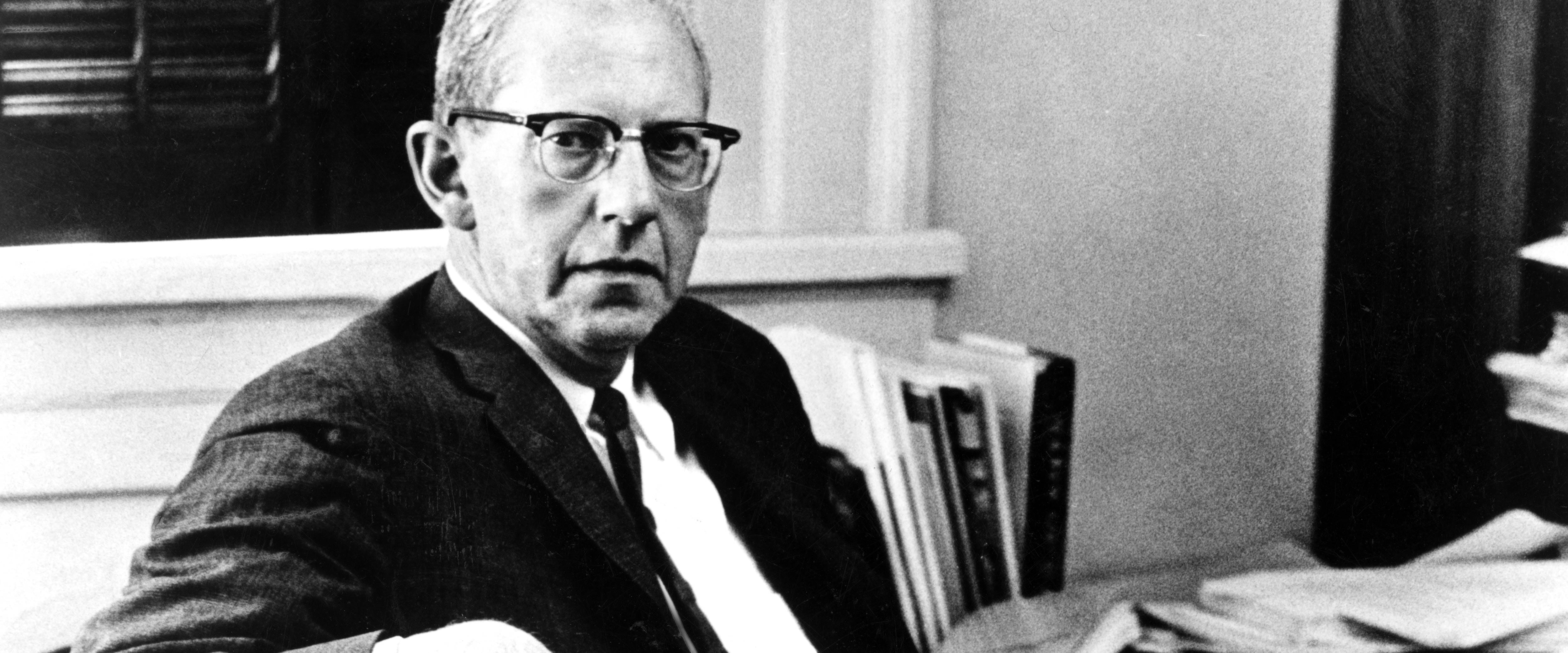 George Stigler seated in a chair looking at the camera