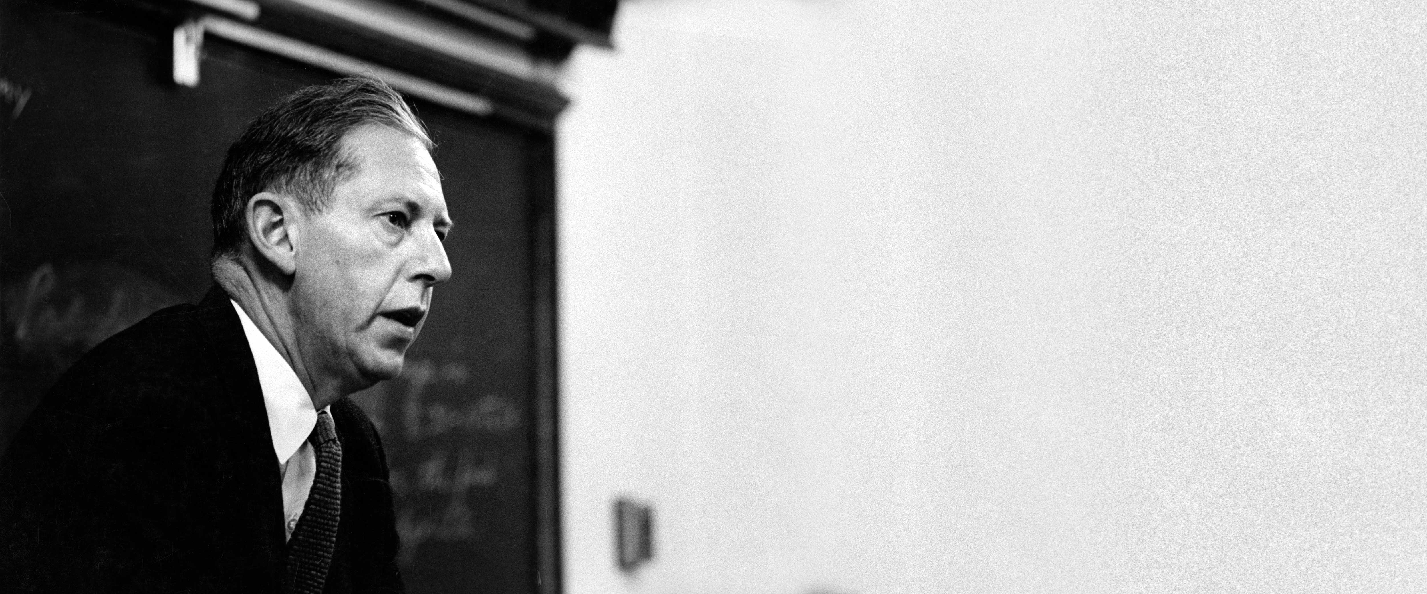 George Stigler speaking in front of a blackboard