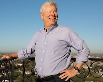 Richard Thaler smiles on his balcony overlooking green trees