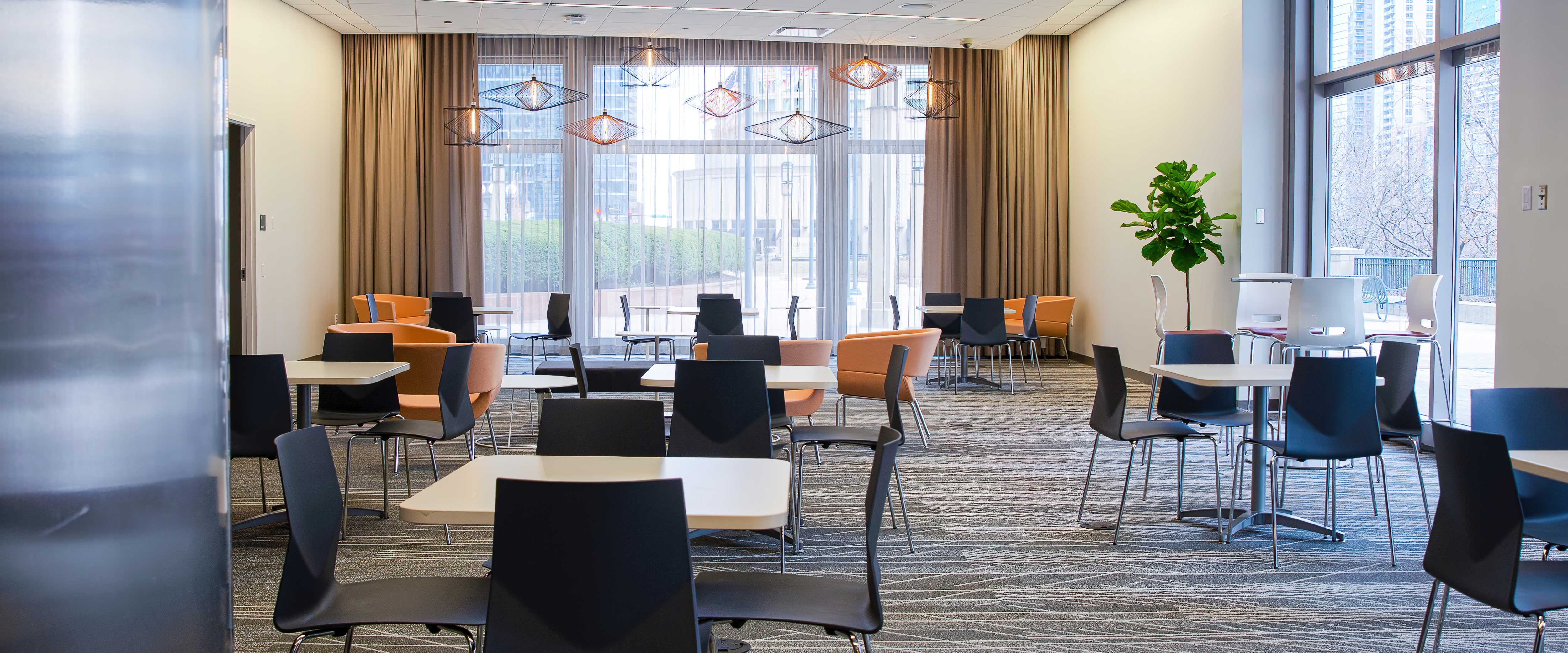 The Gleacher Center lobby lounge with bright windows and angular lighting fixtures filled with tables and chairs