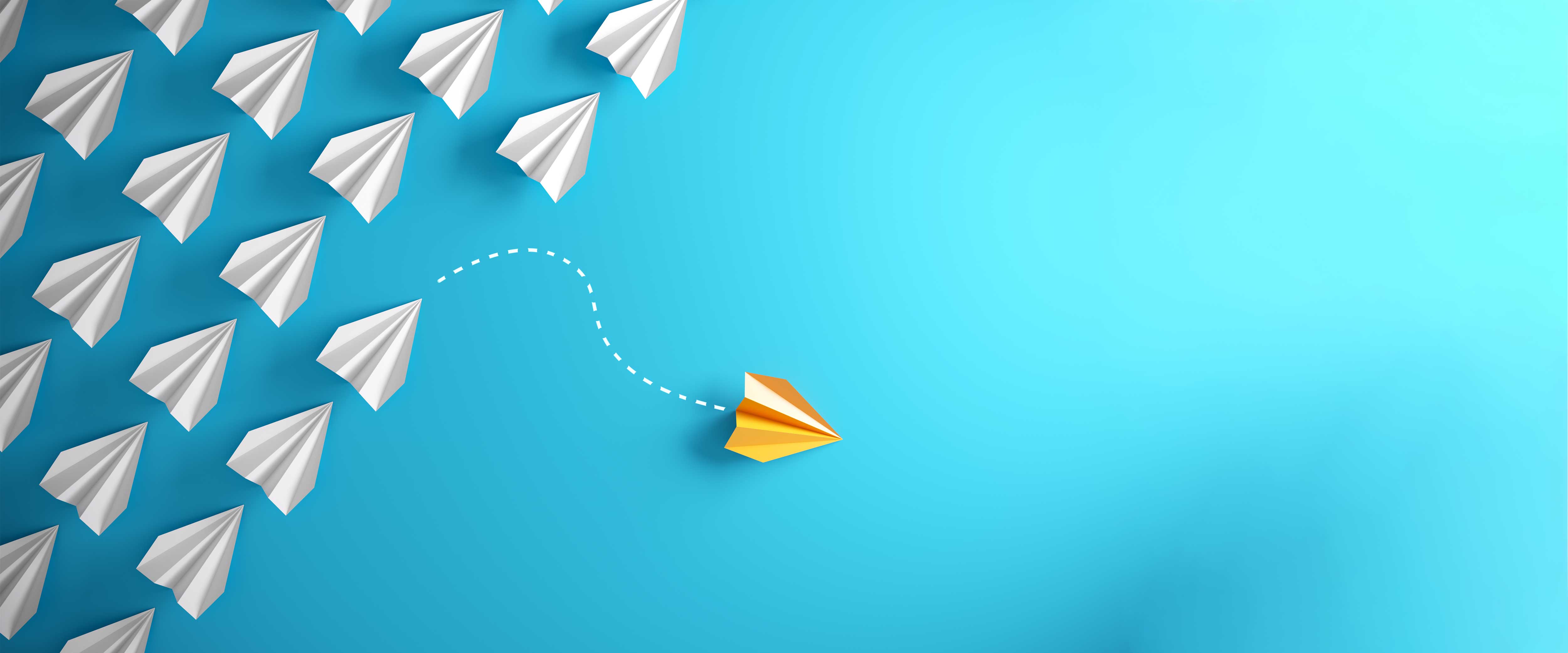 Paper airplane in yellow flying away from white paper airplanes