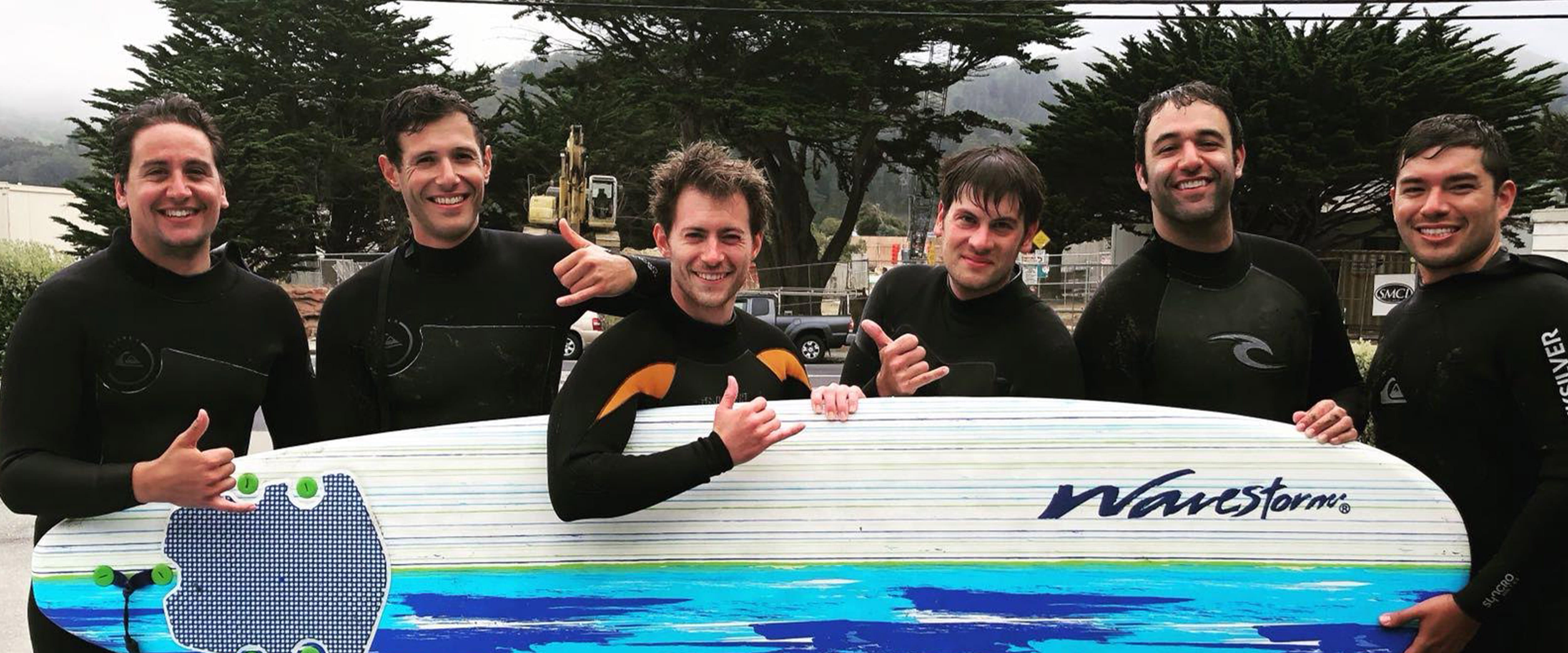 group of surfers posing with a surf board