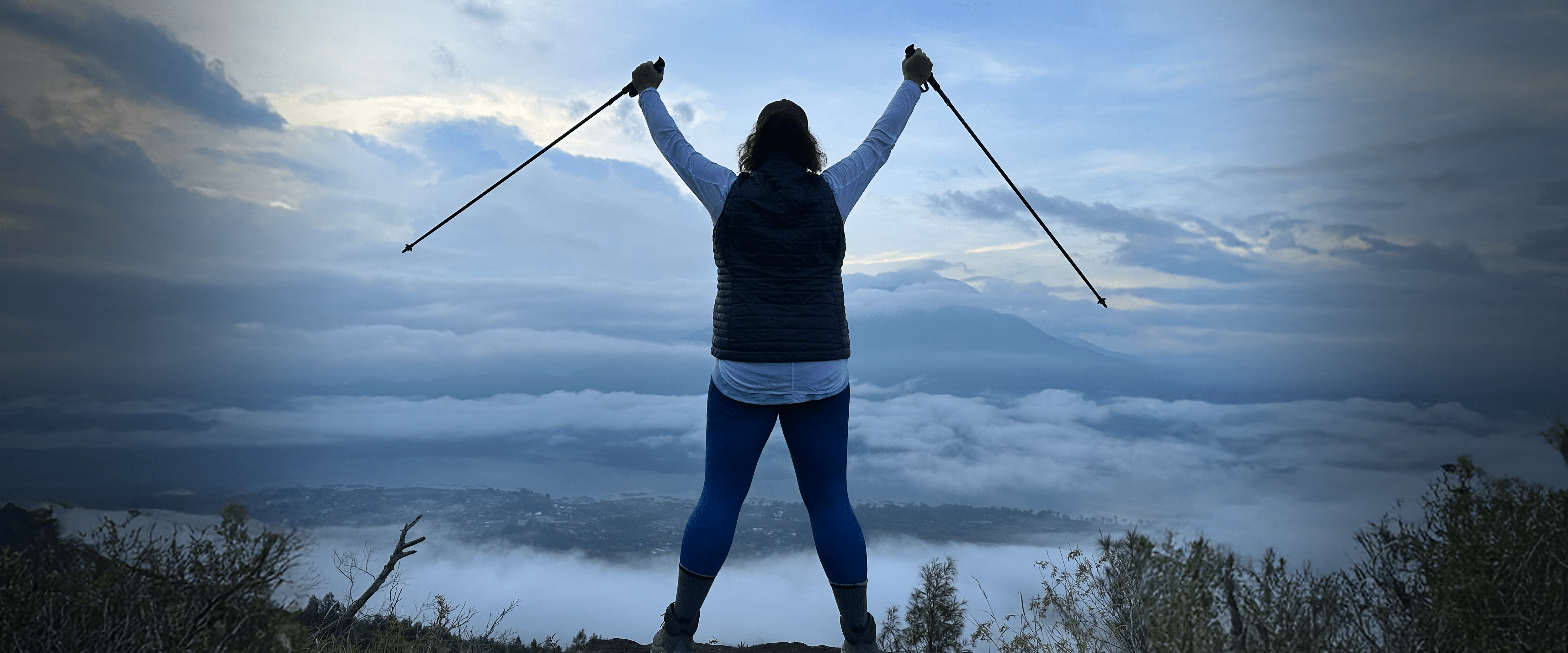 Kate Volzer, from behind, raising her hiking poles on a mountain.