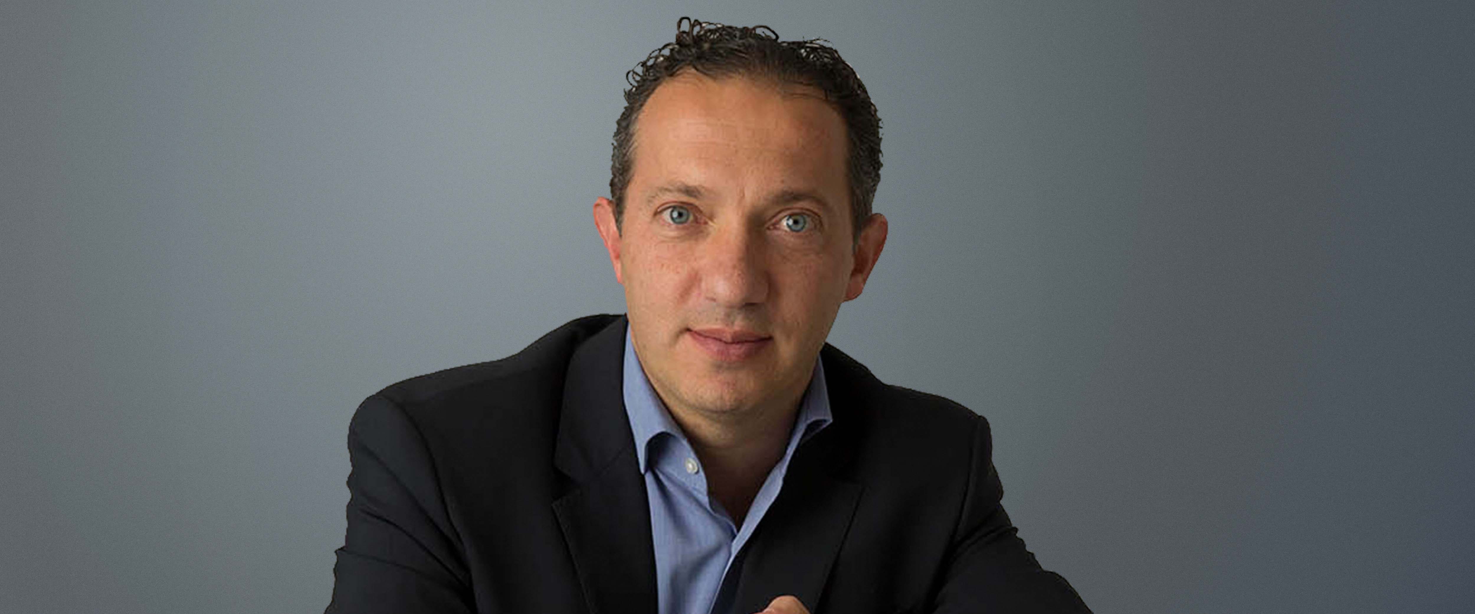 Black and white headsot of Costa Economou, ’10 (EXP-15) in front of a gray background