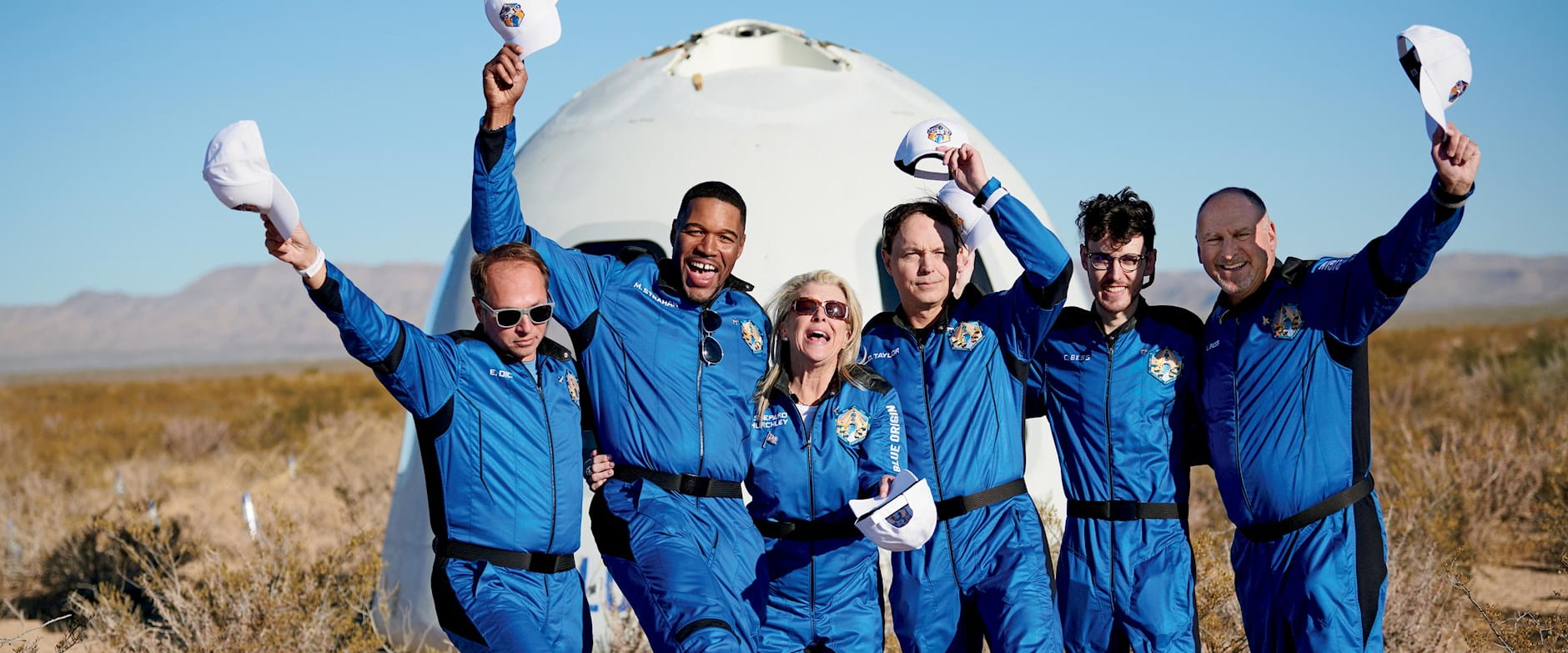 Six people in blue uniforms standing in front of a space vehicle