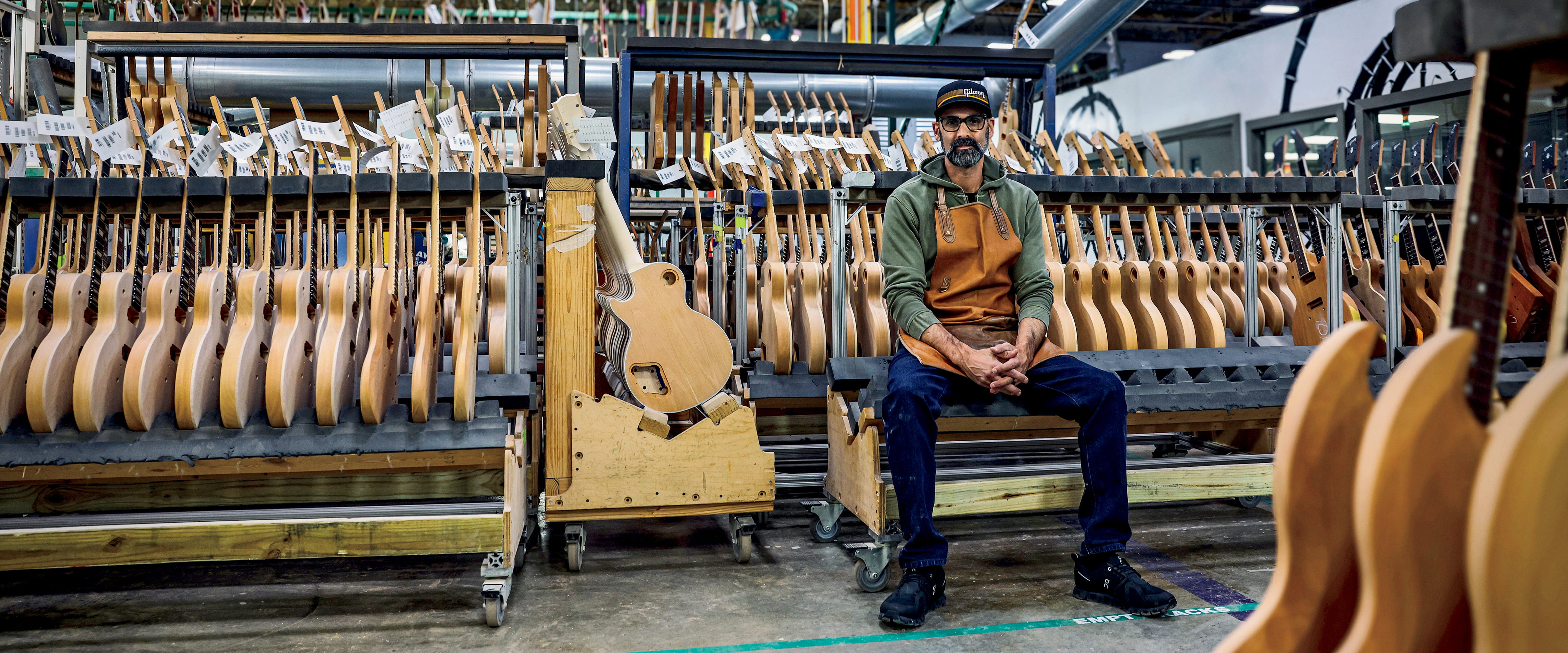 Cesar Gueikian sitting in front of a rack of guitars.