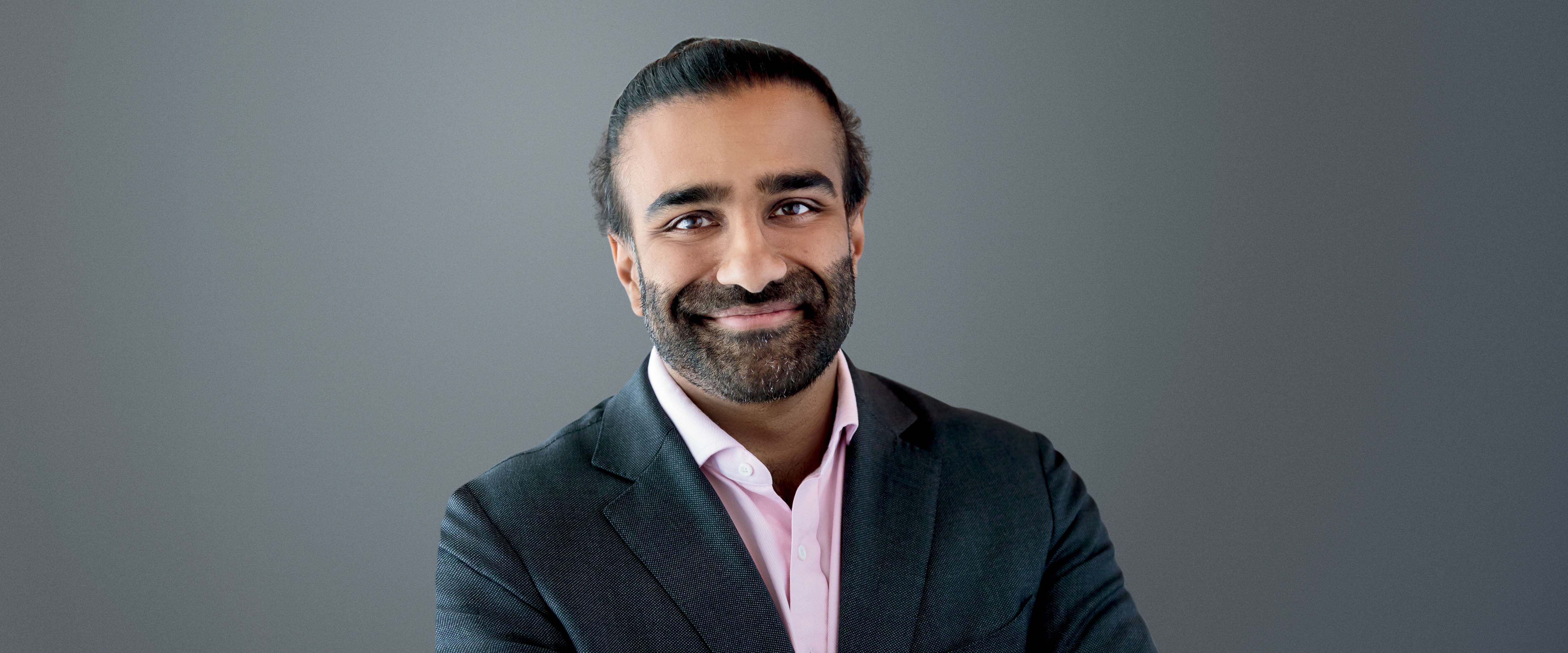 Raghu Betina, AB ’13 in front of a gray background.