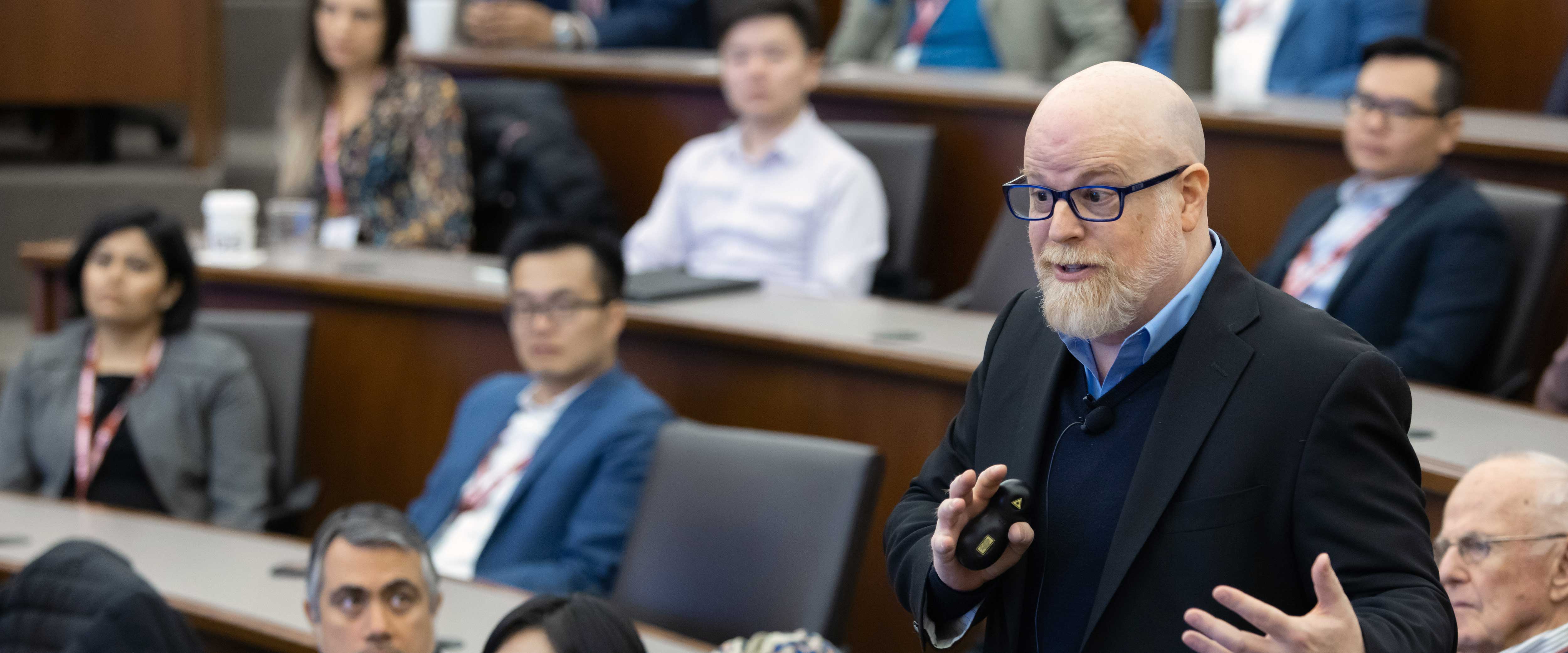 Hurst giving a talk with audience members listening in the background