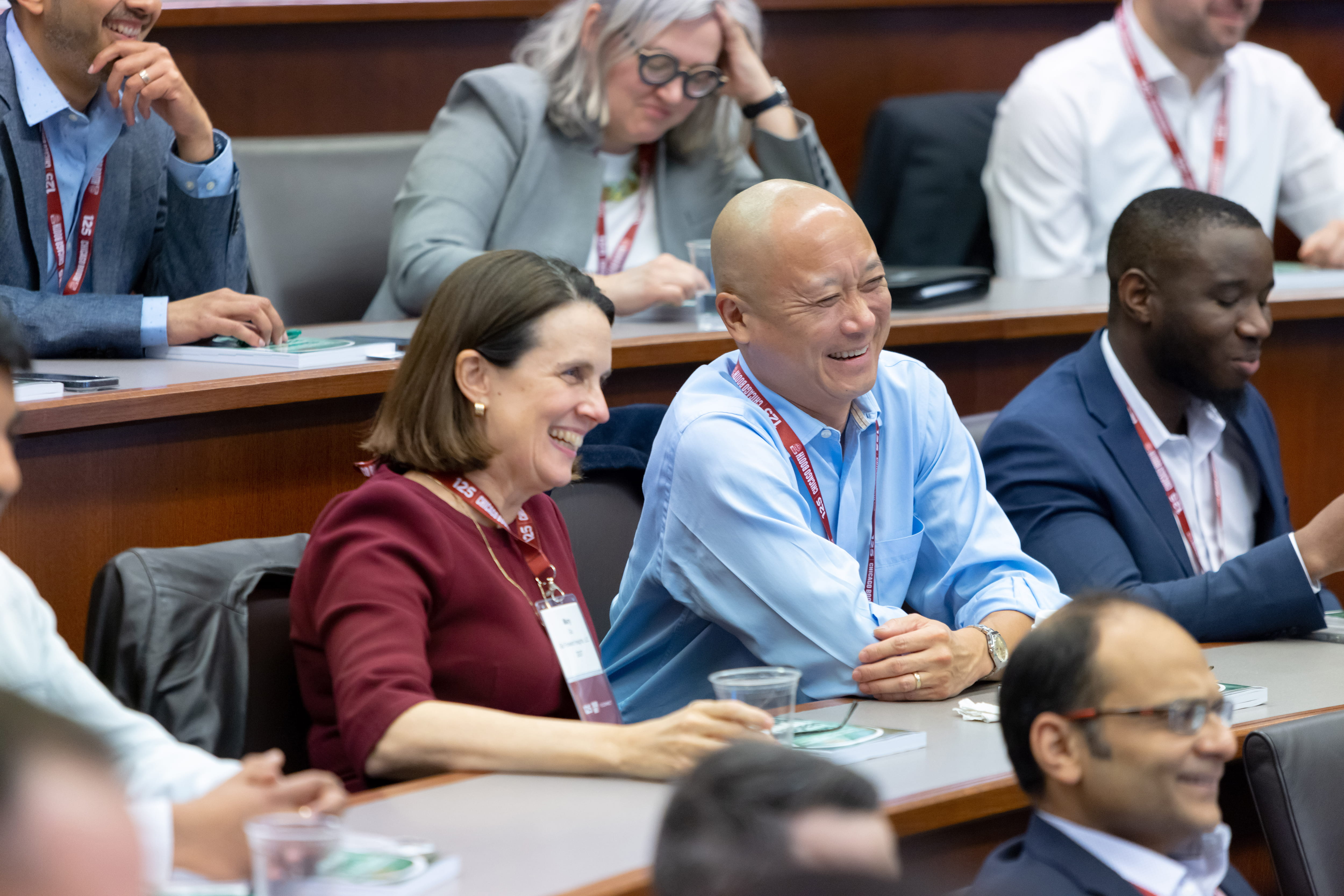 A man and woman smile while watching a lecturer in a crowded classroom.
