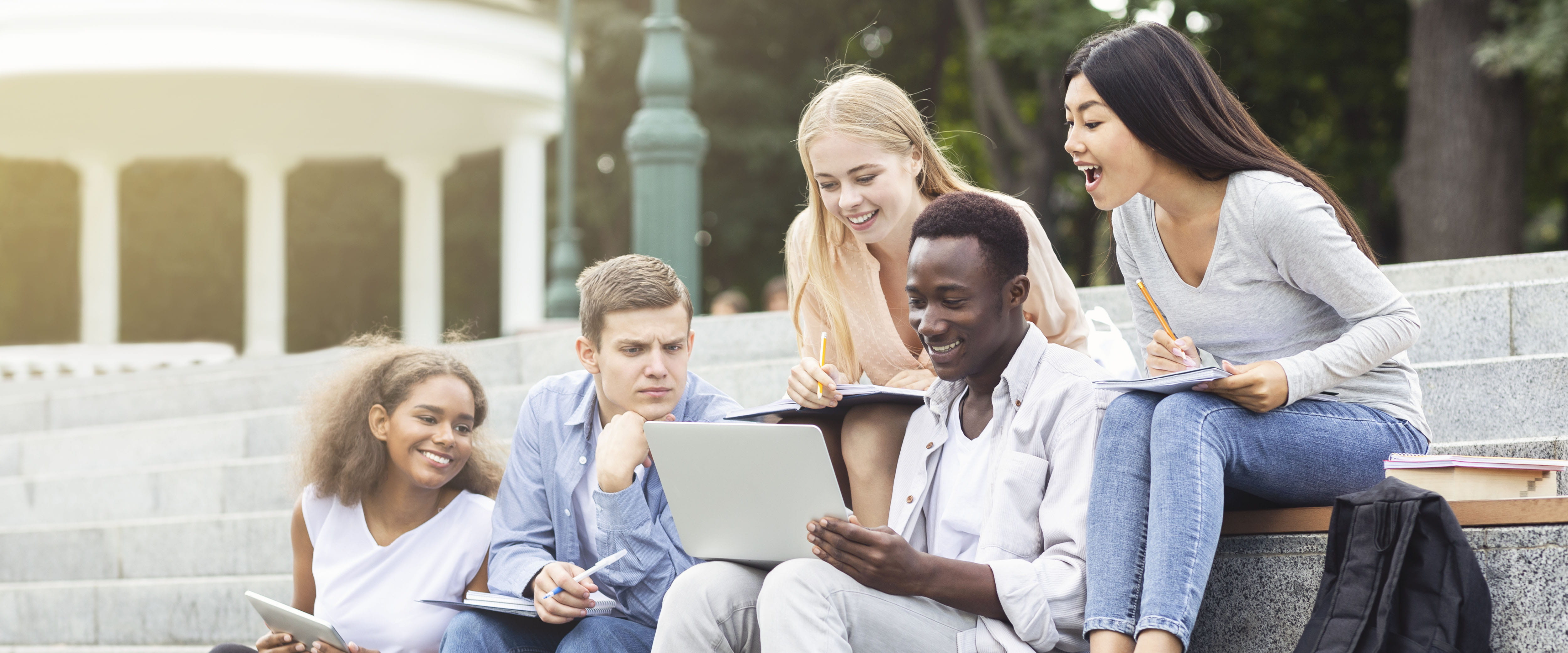 Five finance students looking at a laptop while sitting on stairs