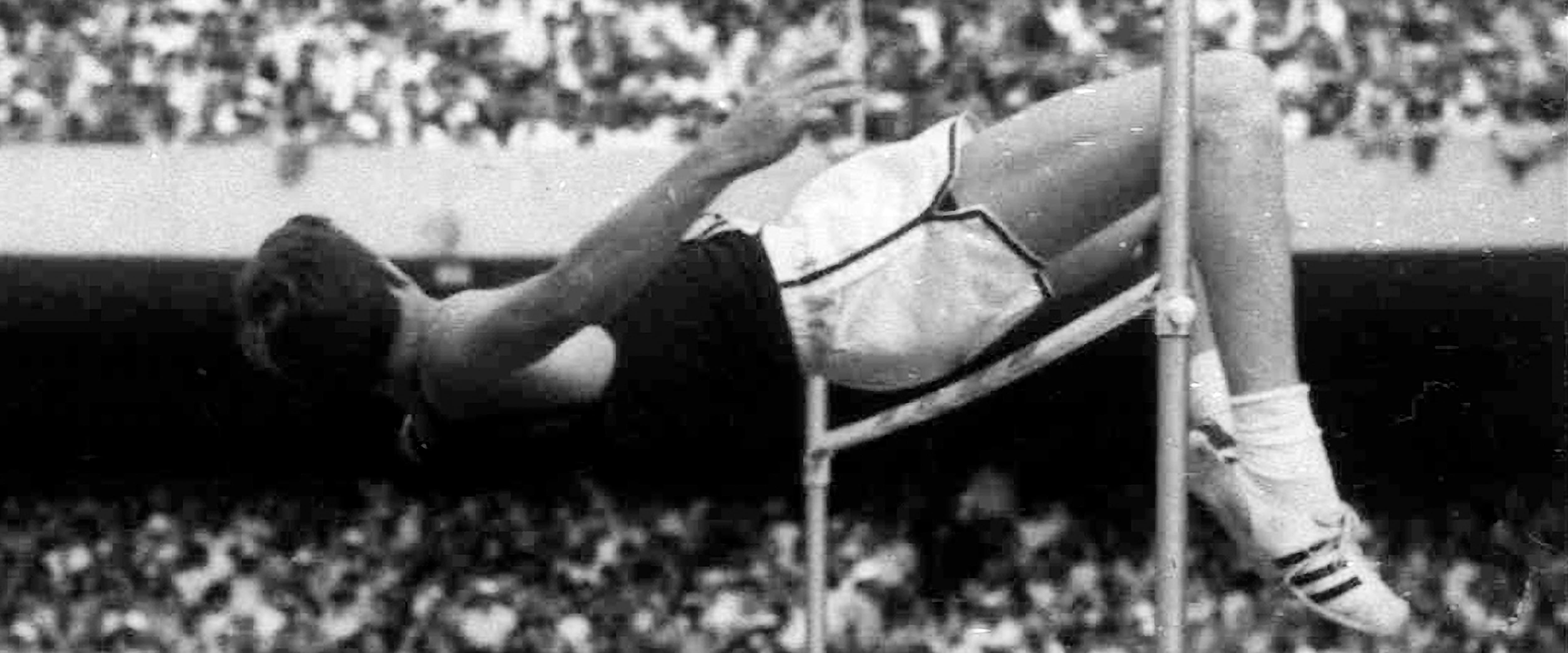 Historical photograph of an athlete soaring over the high jump at a competition.