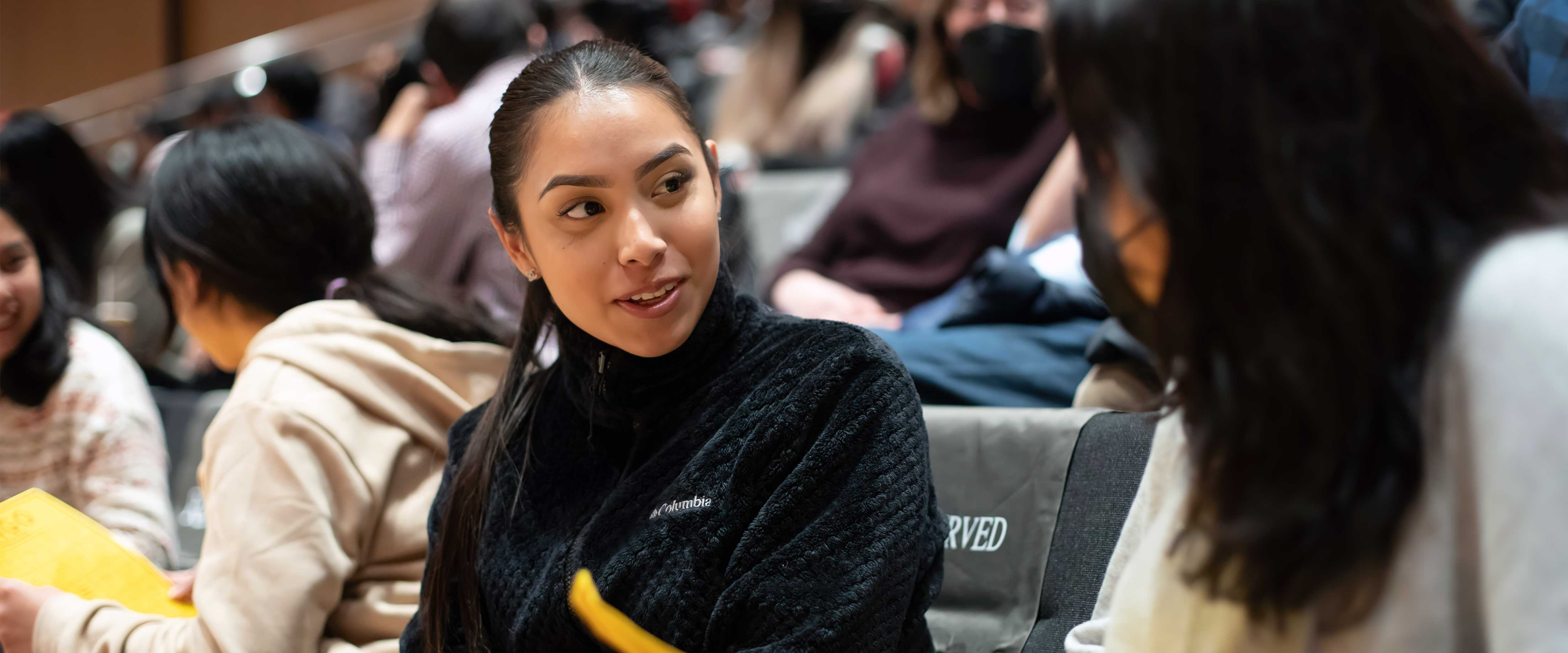 Chicago Booth female student speaking to another student in an auditorium