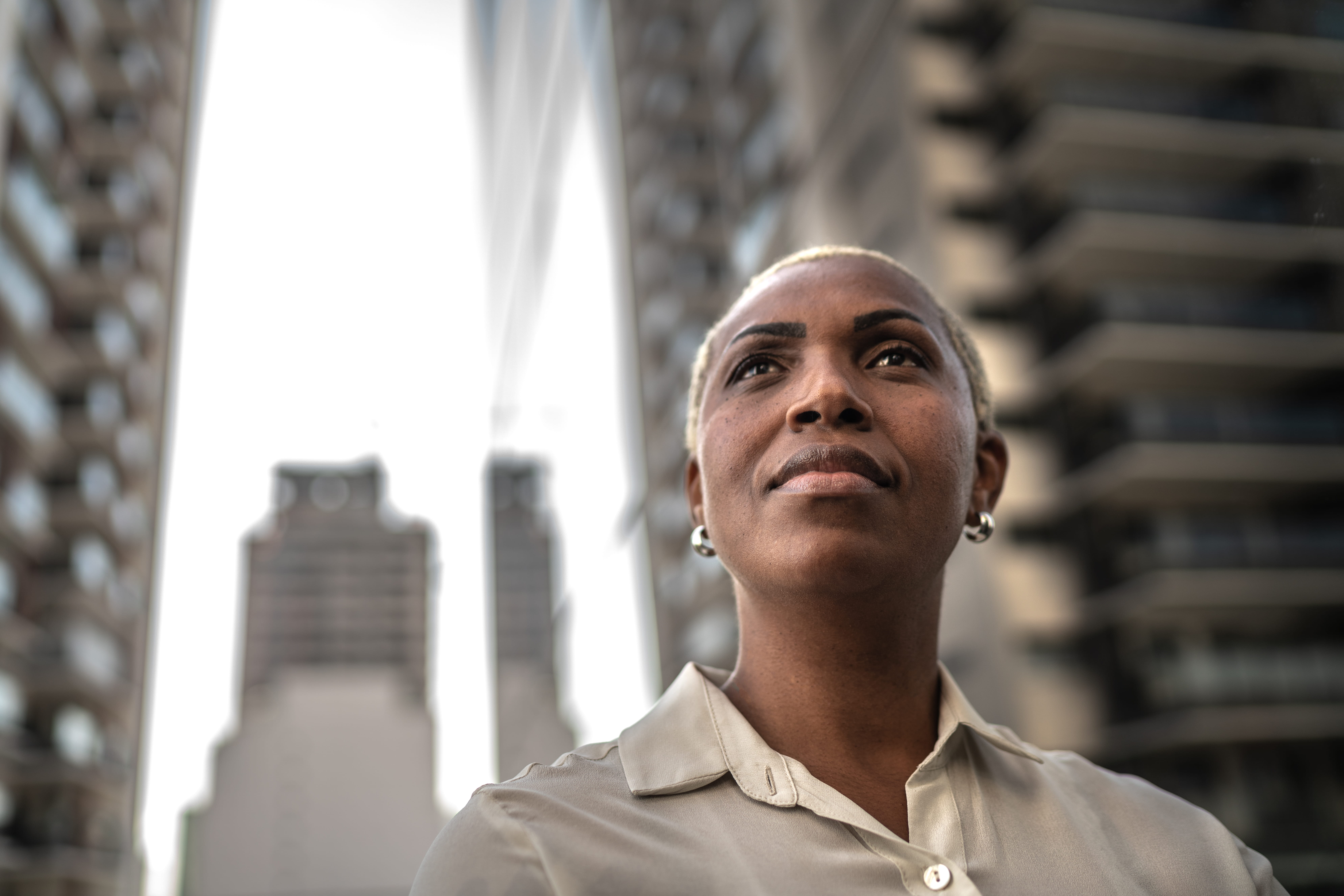 Woman looking up with tall buildings behind her