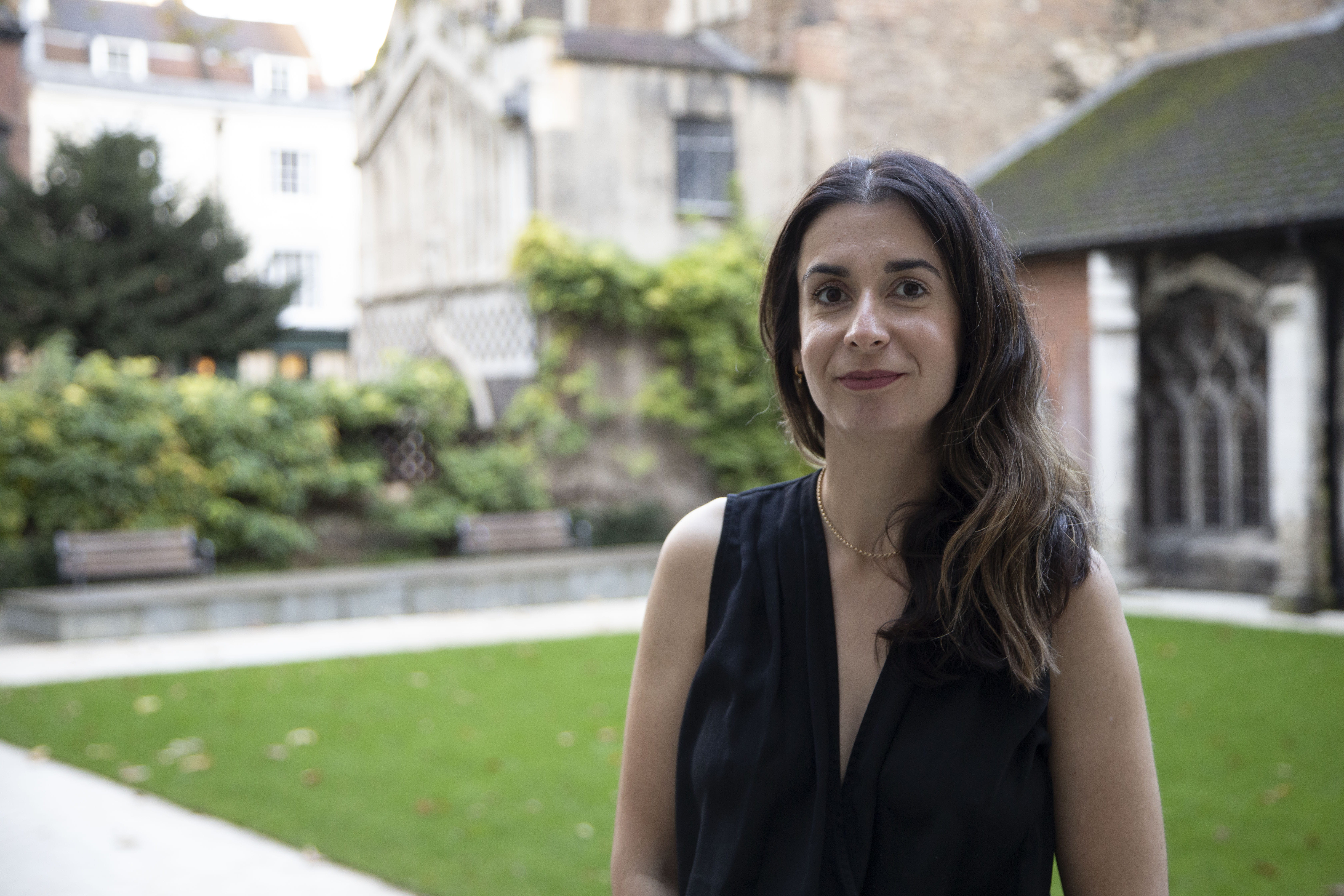 A woman standing in front of a lawn and buildings and smiling at the camera