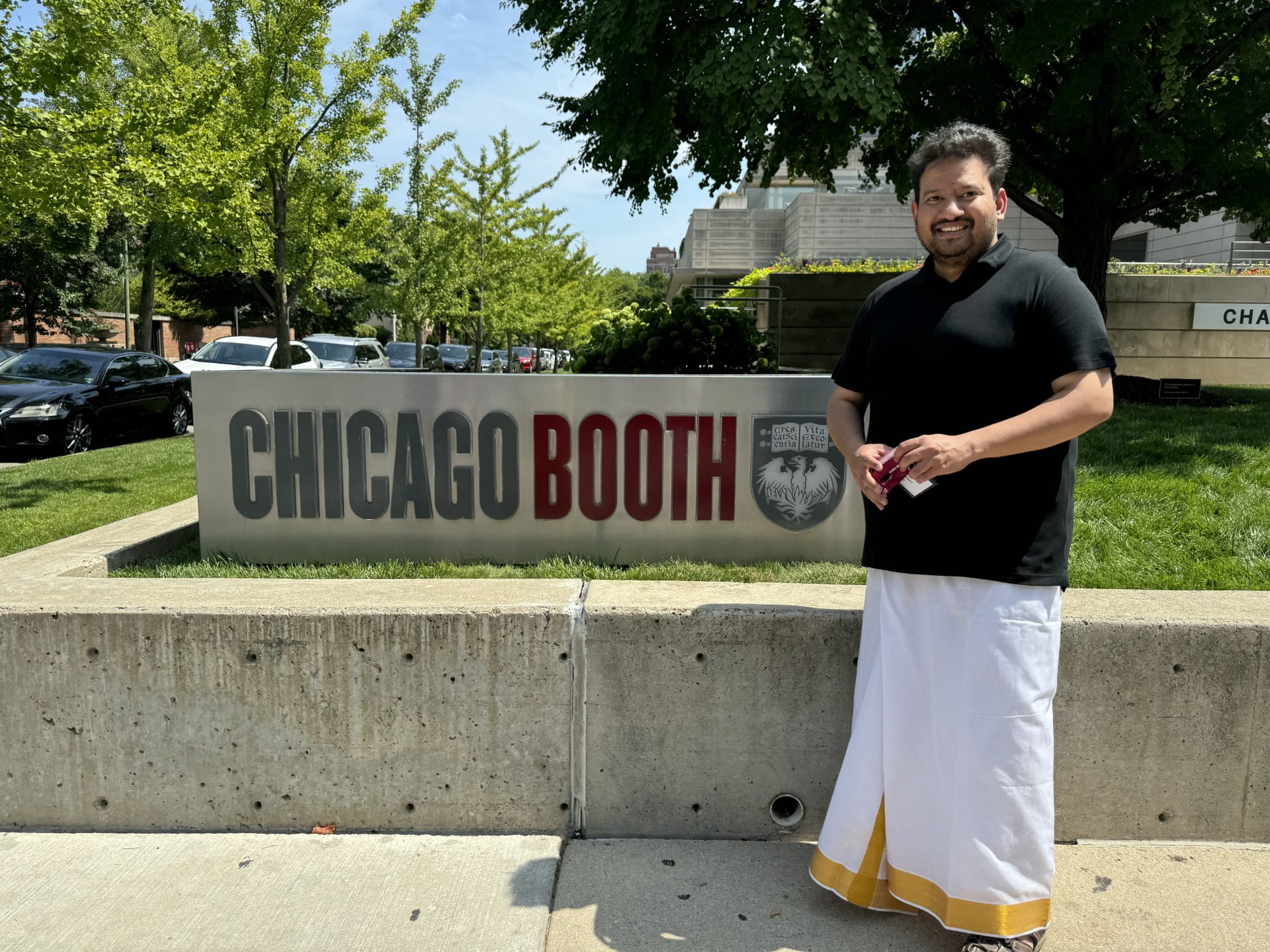 A man standing next to a Chicago Booth sign and smiling at the camera