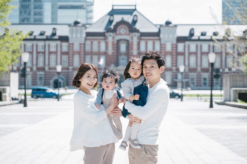 A man and a woman hold two small children in front of a large building