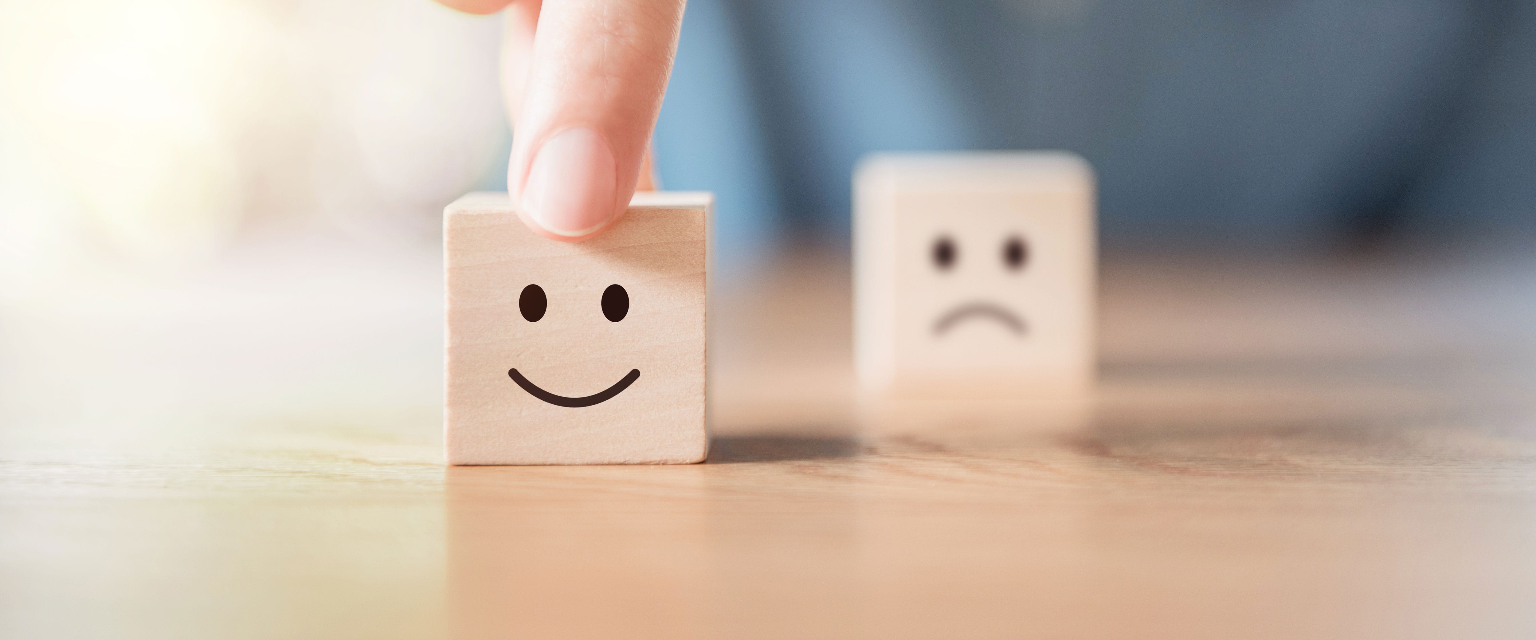 A man pushes a wooden block with a smilley face on it while a frowny face block is out of focus in the background