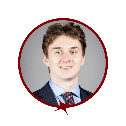 Picture of auburn-haired man in a blue tuxedo and tie standing in front of a grey background
