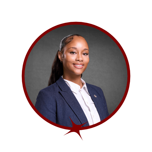 Picture of dark-haired smiling woman in a blue blazer and white undershirt in front of a grey background. 