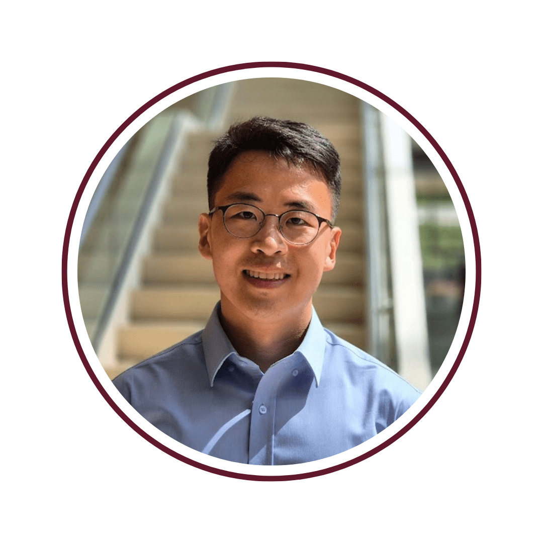 Young man with dark hair and glasses standing in front of a tall, tile staircase. He is wearing a light blue button-up shirt. 