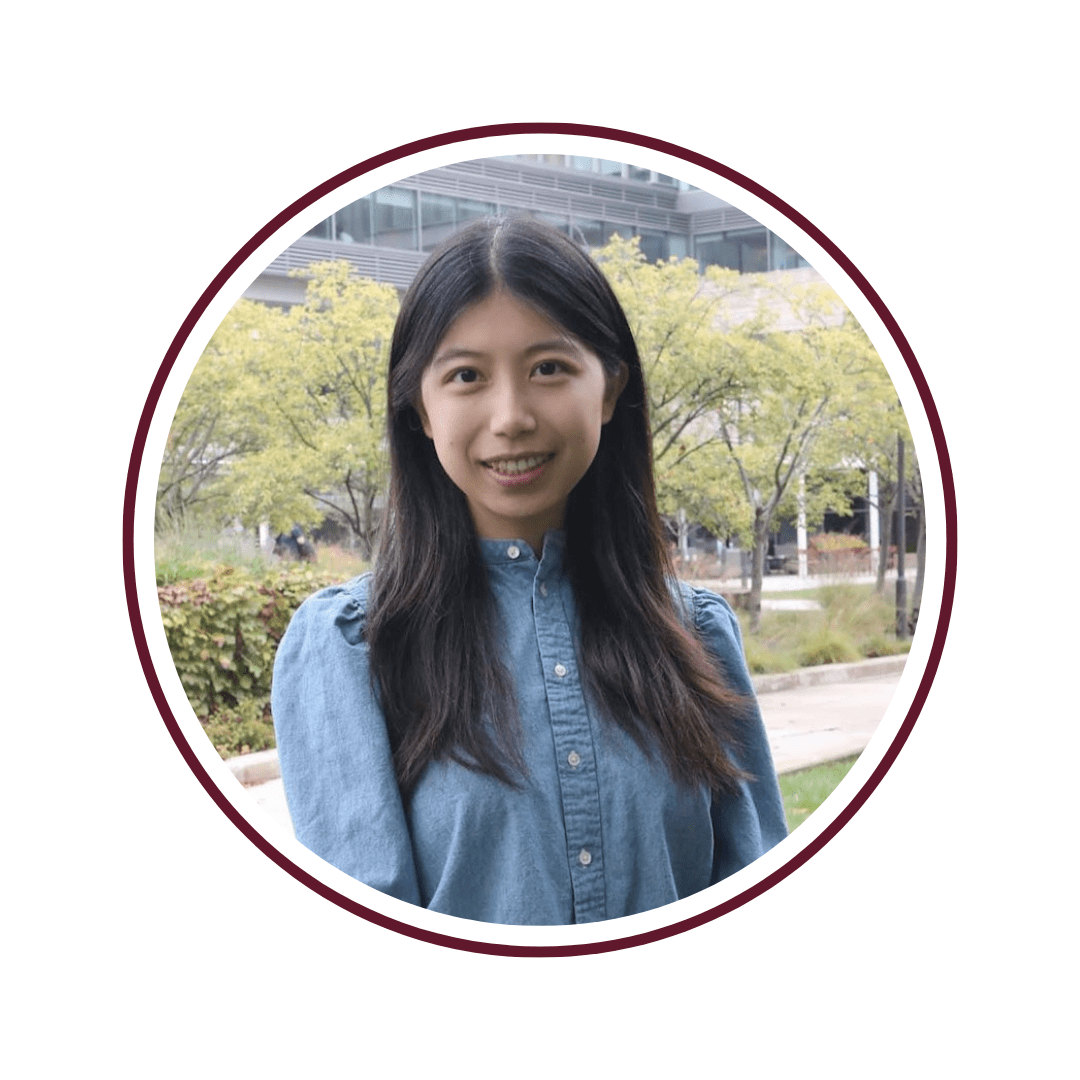 Young woman standing in front of green foilage and a building atrium. She has dark hear and is wearing a long-sleeved blue shirt with white buttons. The picture is bordered by a maroon circle frame.