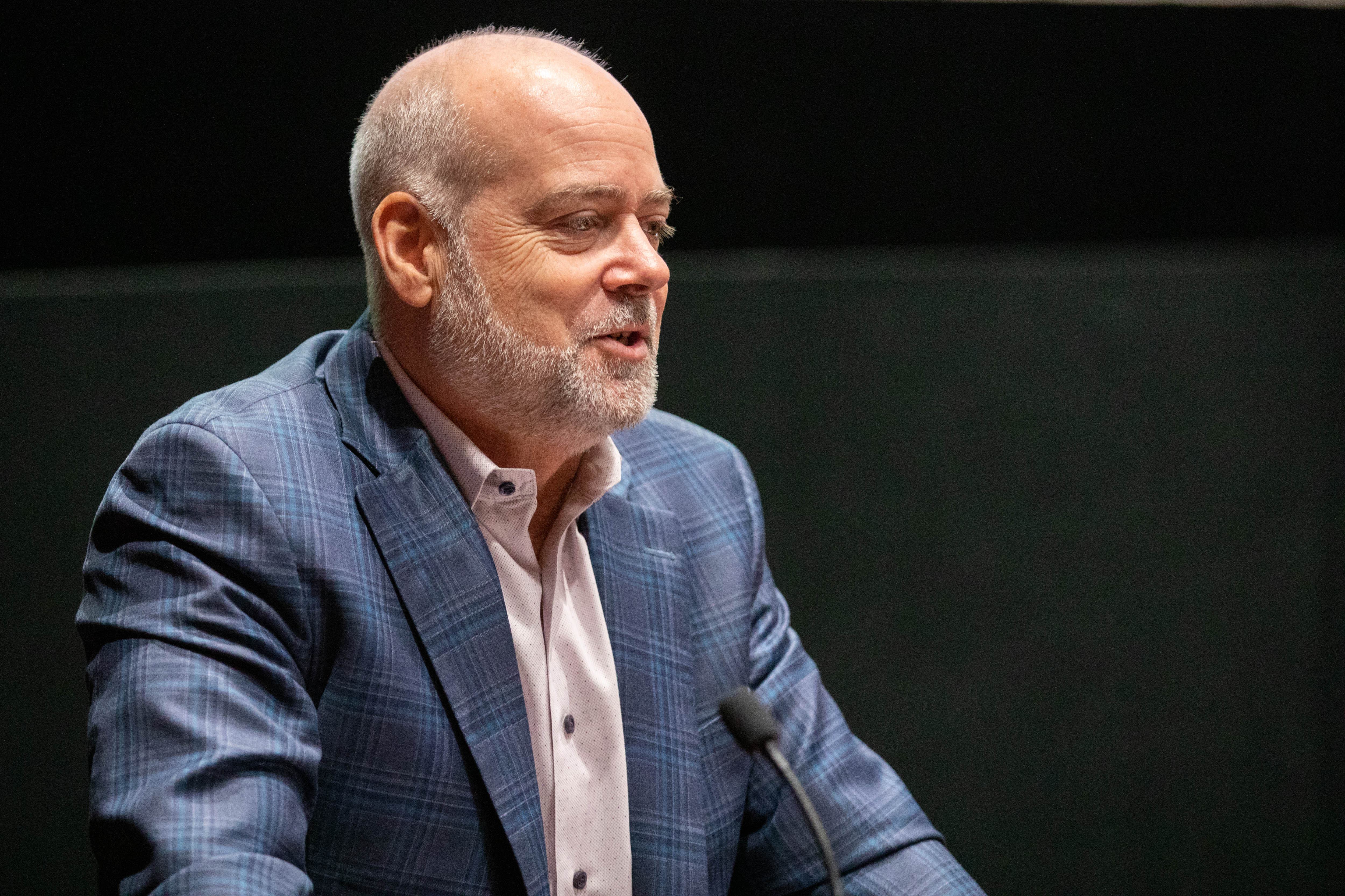 Jeffrey R. Russell wearing a blue blazer with a dotted shirt underneath it, speaking to an audience