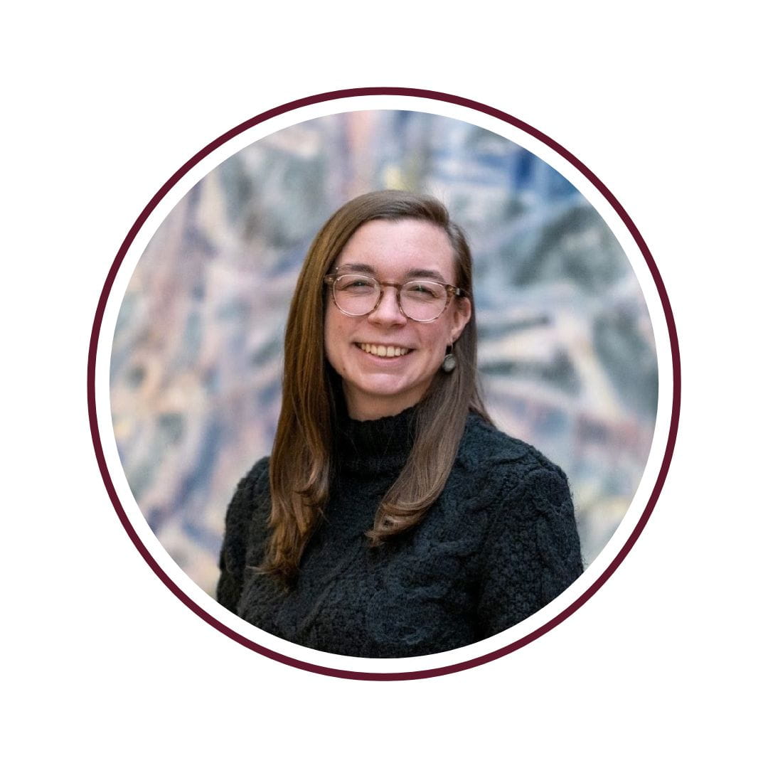 A smiling woman wearing a black turtleneck standing in front of a blurred background. The photo is bordered by a maroon circle. 