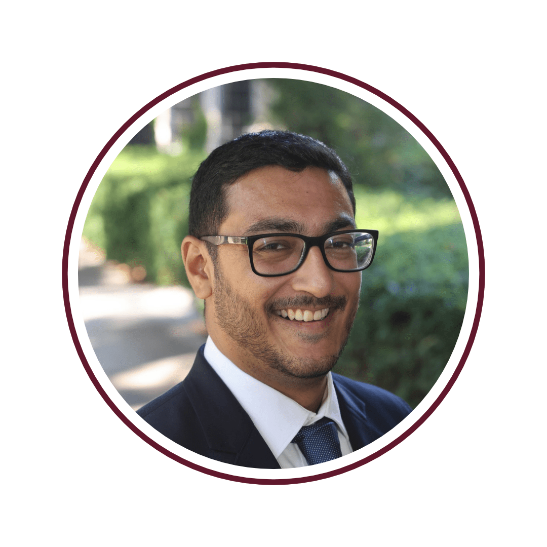 A young man with short black hair, glasses, a black blazer, and a tie.