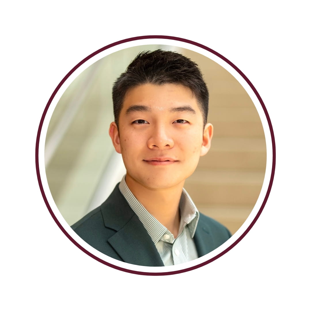 Picture of smiling dark-haired student wearing a tuxedo and standing in front of a marble staircase. The picture is bordered by a maroon circle frame. 