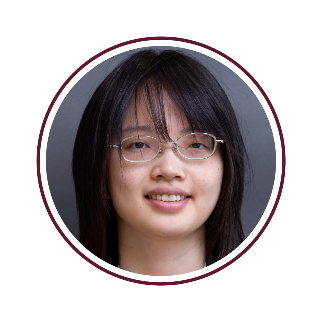Picture of smiling dark-haired woman wearing glasses and standing in front of a grey background. The picture is bordered by a maroon circle. 