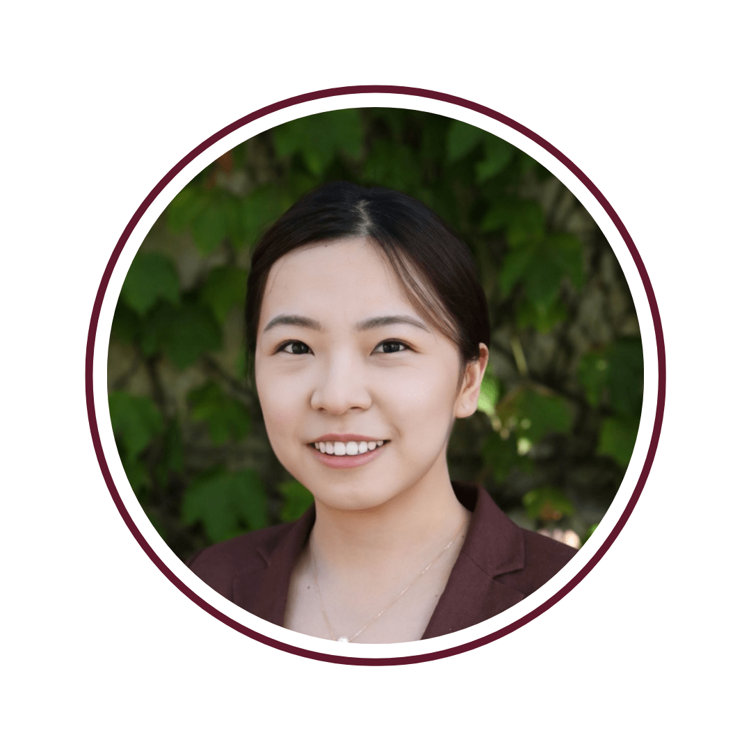 Picture of smiling, dark-haired young woman in front of green vines. She is wearing a burgundy blouse. The picture is bordered by a maroon circle. 