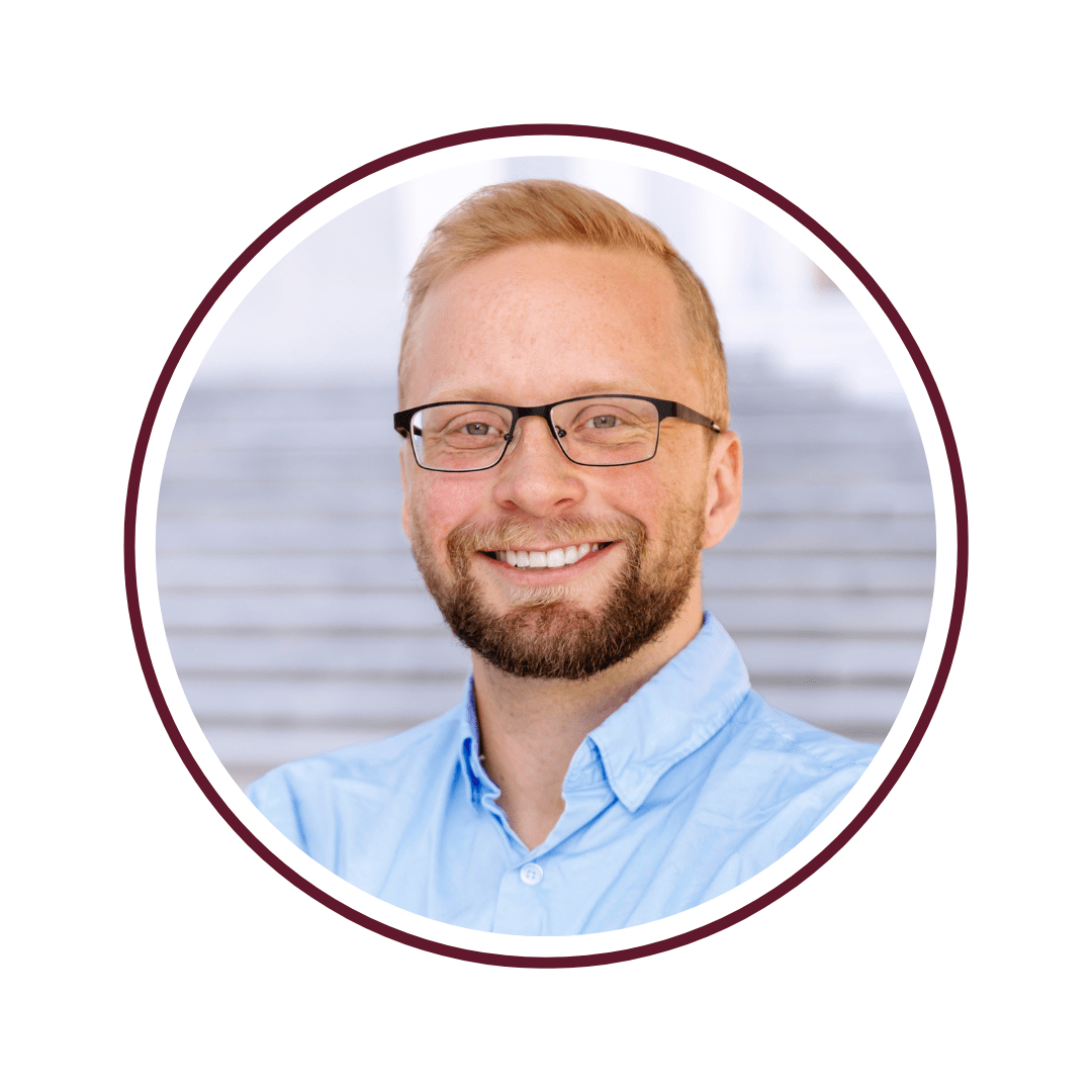 Picture of smiling, ginger-haired man wearing glasses and a light blue button shirt. 