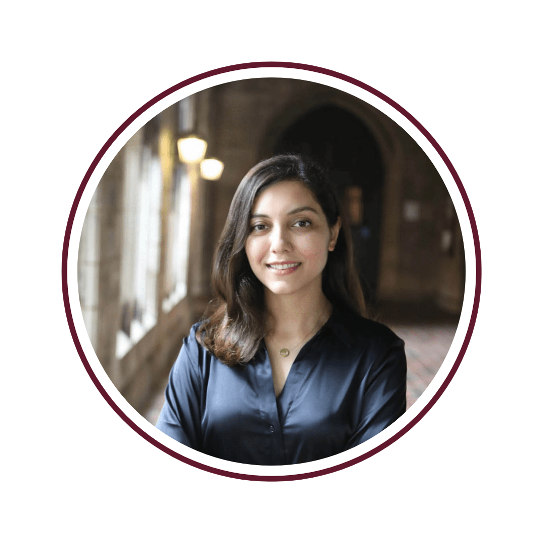 Picture of dark-haired smiling woman wearing a silk blouse and standing in front of a sun-lit archway