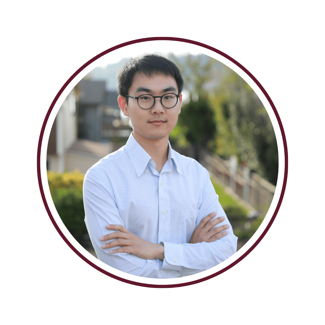 Young man wearing glasses and a light blue button down shirt stands in front of a blurred green background 