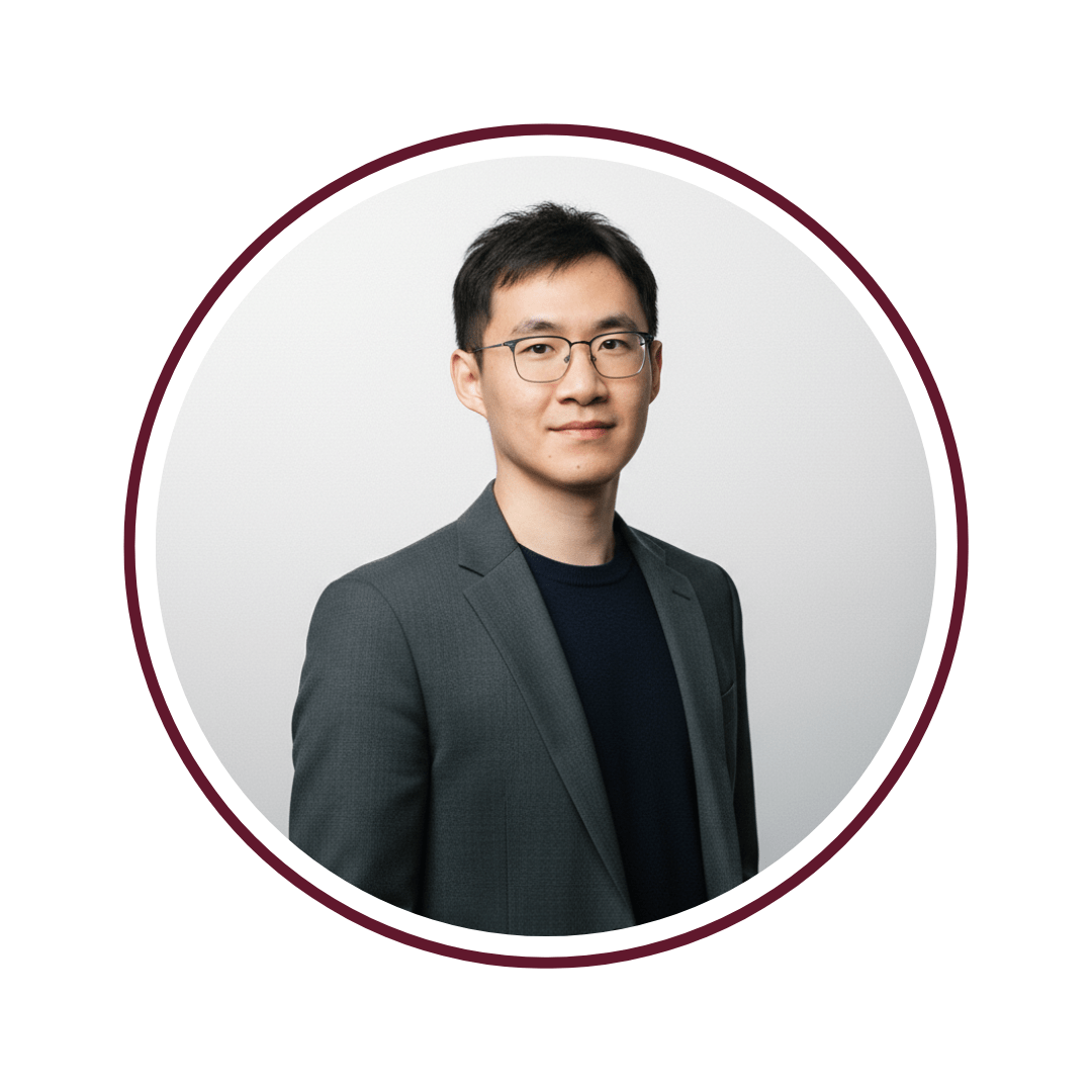 Picture of dark-haired, smiling man in a grey blazer standing in front of a grey background