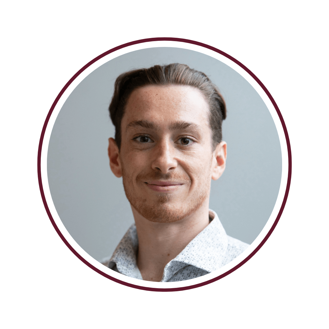 Picture of ginger-haired, smiling young man in a white and blue dress shirt. The background of the photo is grey. 